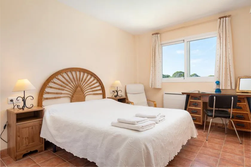 A bedroom with a bed, a desk, and a window with curtains.