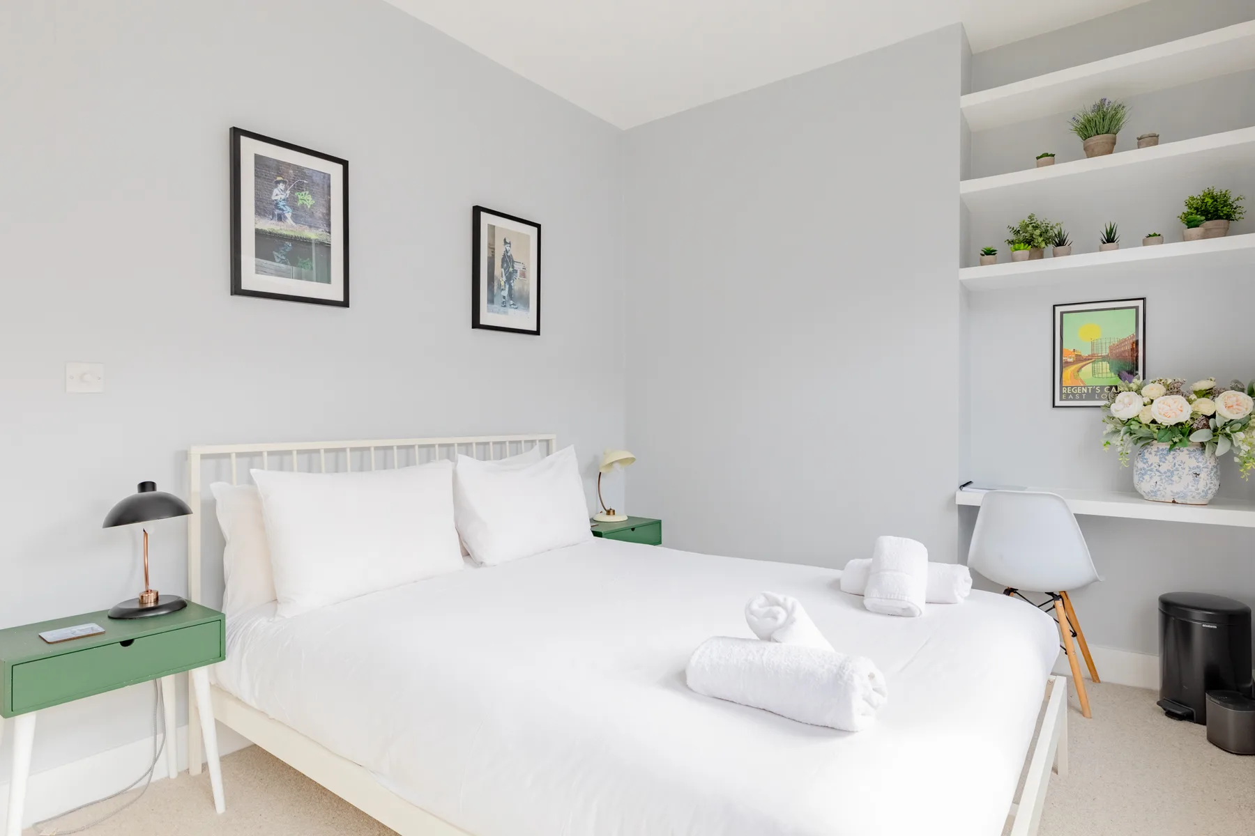 A bright bedroom with white bedding and framed artwork on the walls.