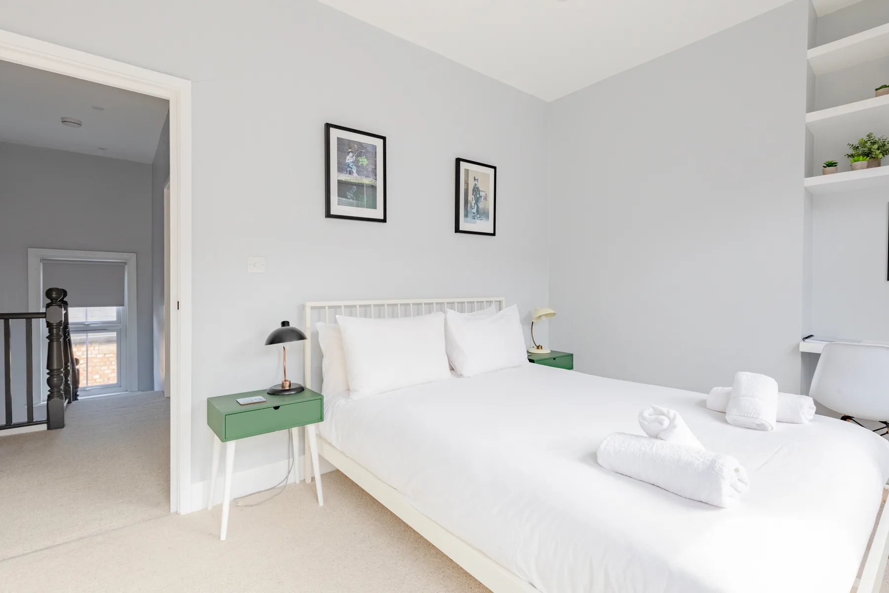 A bright bedroom with white bedding and framed pictures above the bed.