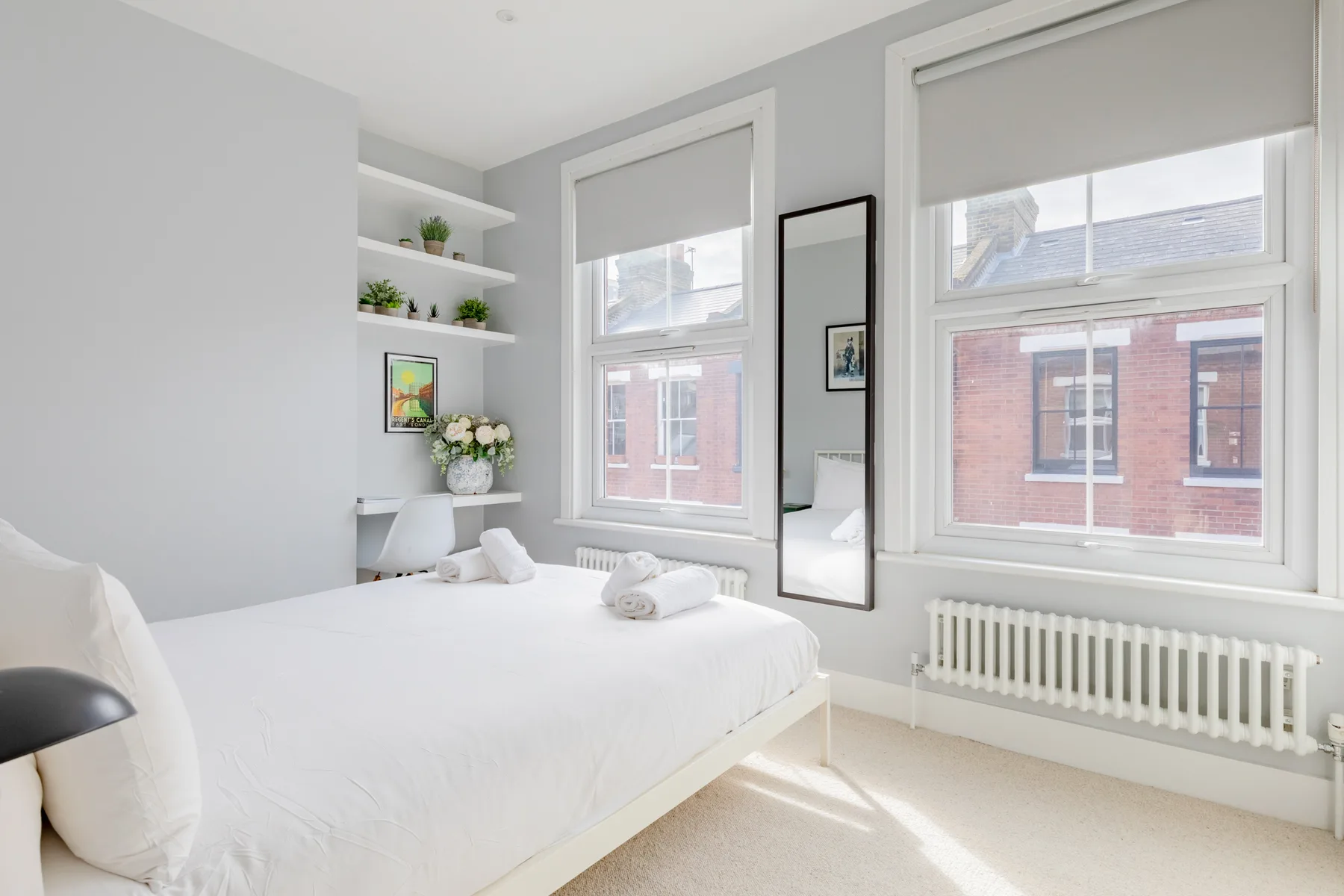 A bright bedroom with a white bed, large windows, and a radiator.