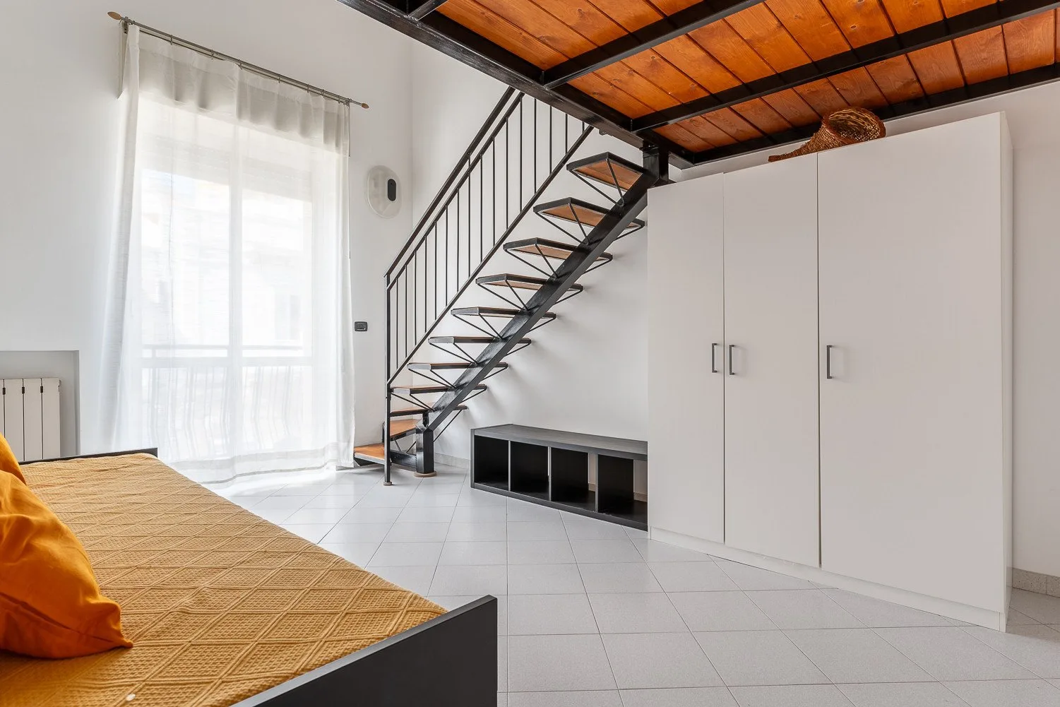 Un dormitorio con una cama bajo una escalera metálica y un techo de madera.