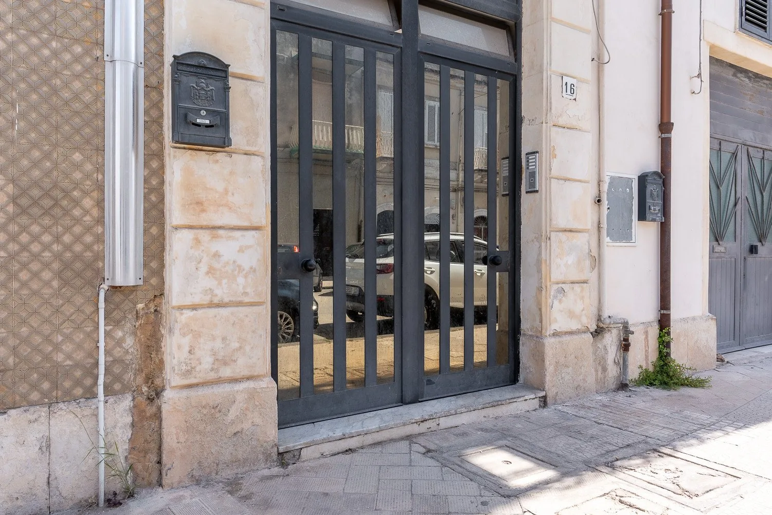 Una entrada de edificio con portones metálicos oscuros junto a la acera.