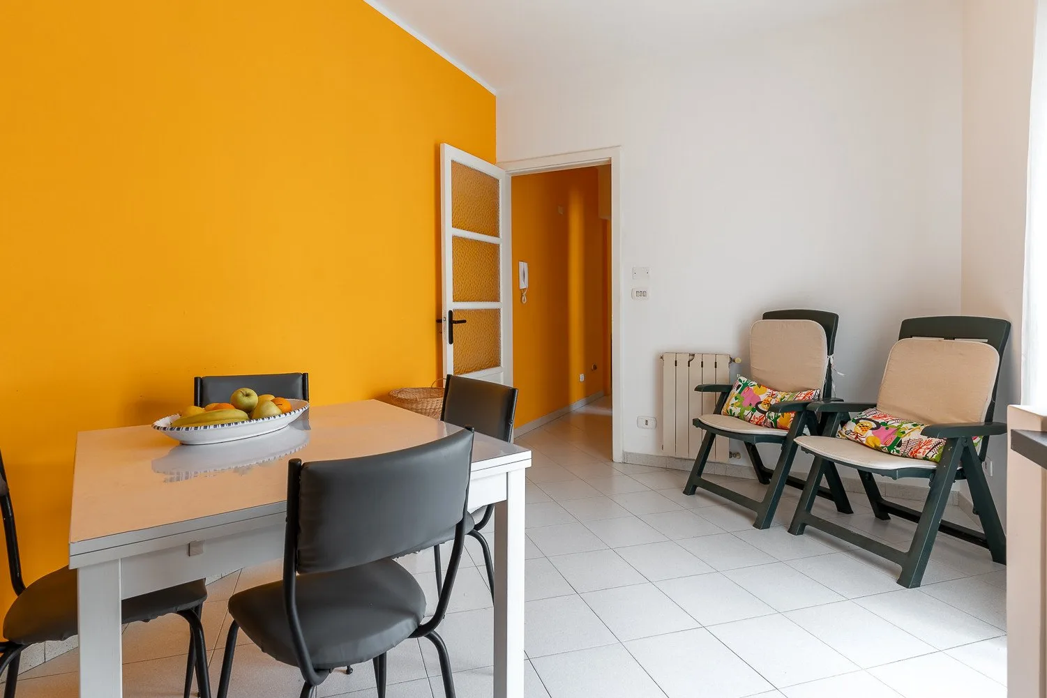 Un comedor con una mesa y dos asientos acolchados junto a una pared naranja.