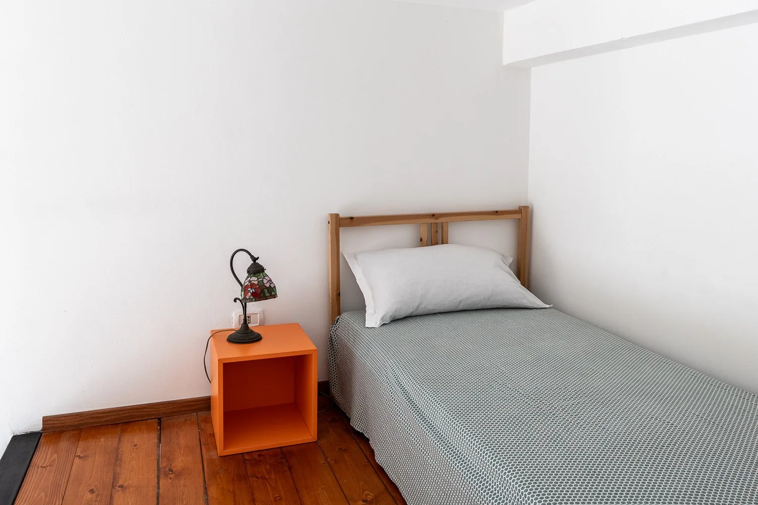 Un dormitorio sencillo con una cama individual y una mesita de noche naranja.