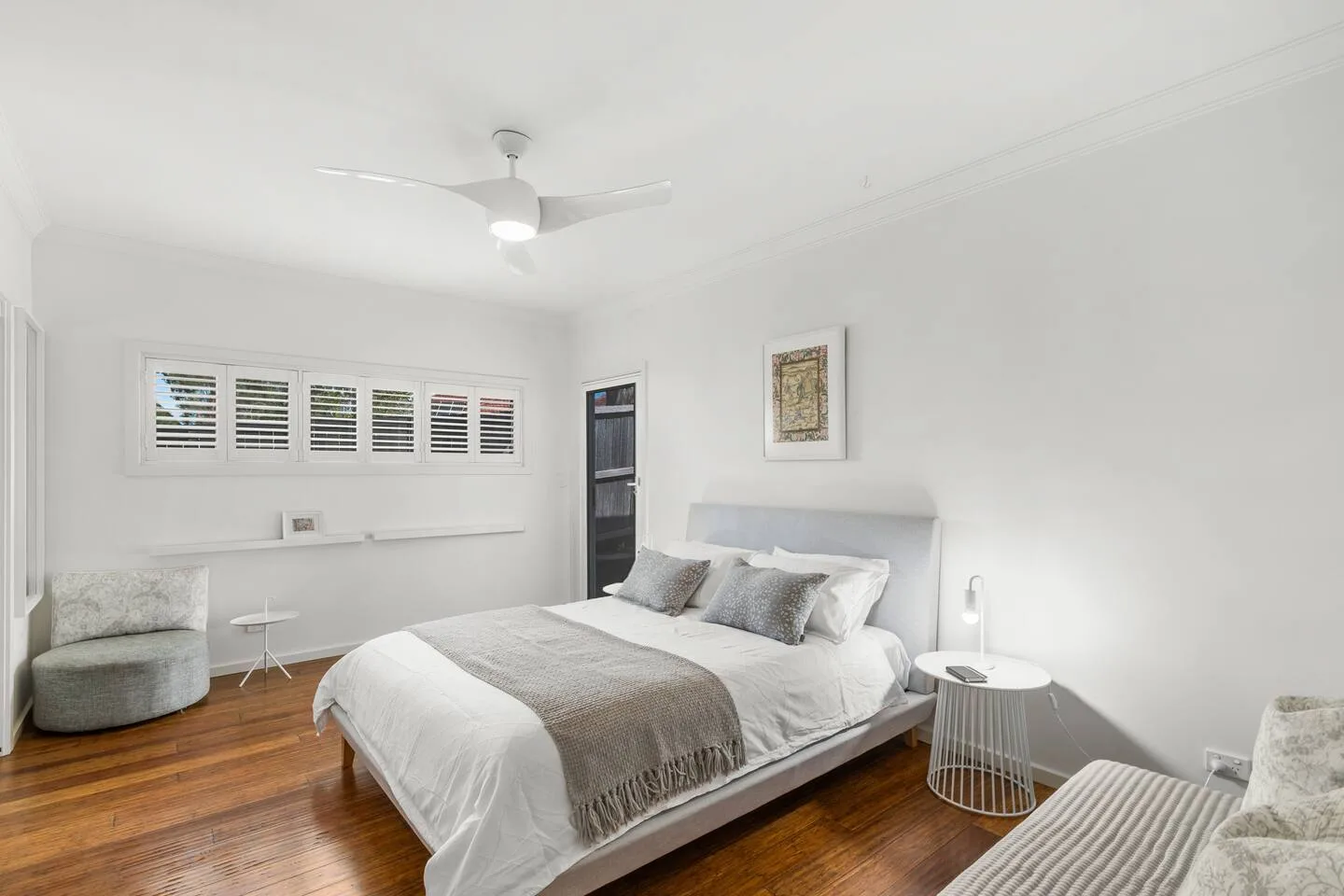 A bright bedroom with a bed, ceiling fan, and seating area.