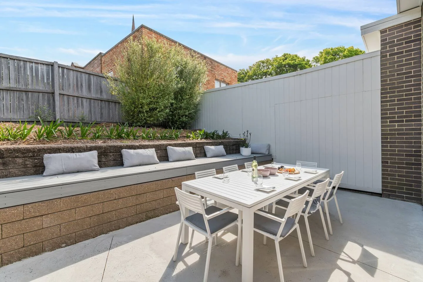Comedor al aire libre con mesa y asientos junto a un jardín elevado.