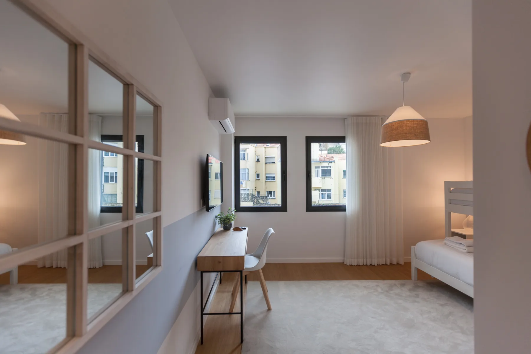 Un dormitorio luminoso con cama, escritorio y ventanas amplias.