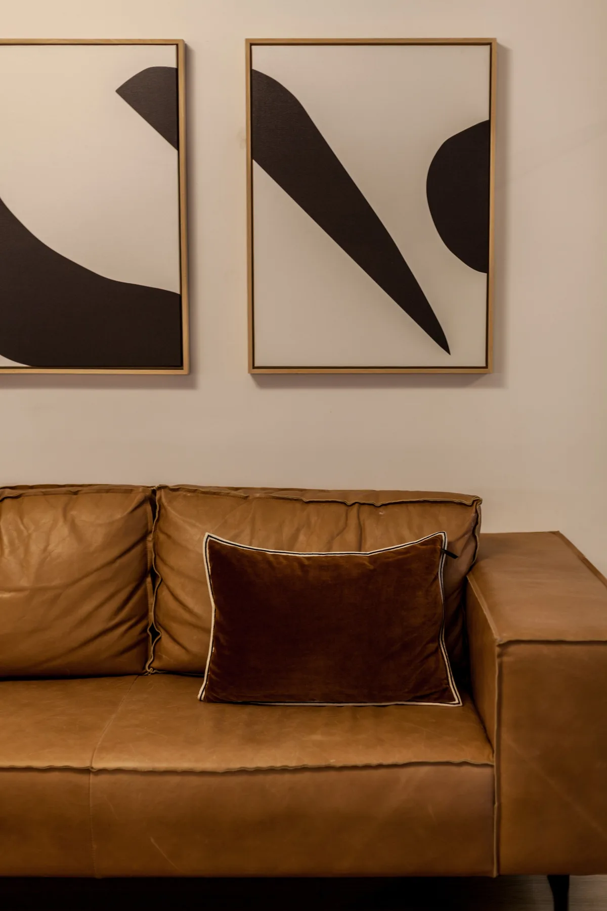 Una sala de estar con asientos marrones bajo dos cuadros abstractos enmarcados.
