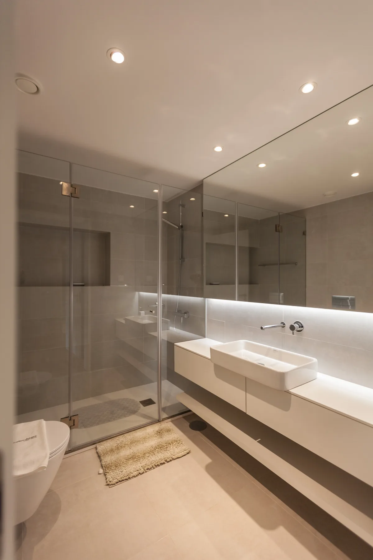 Un baño moderno con ducha de cristal y un largo lavabo blanco.