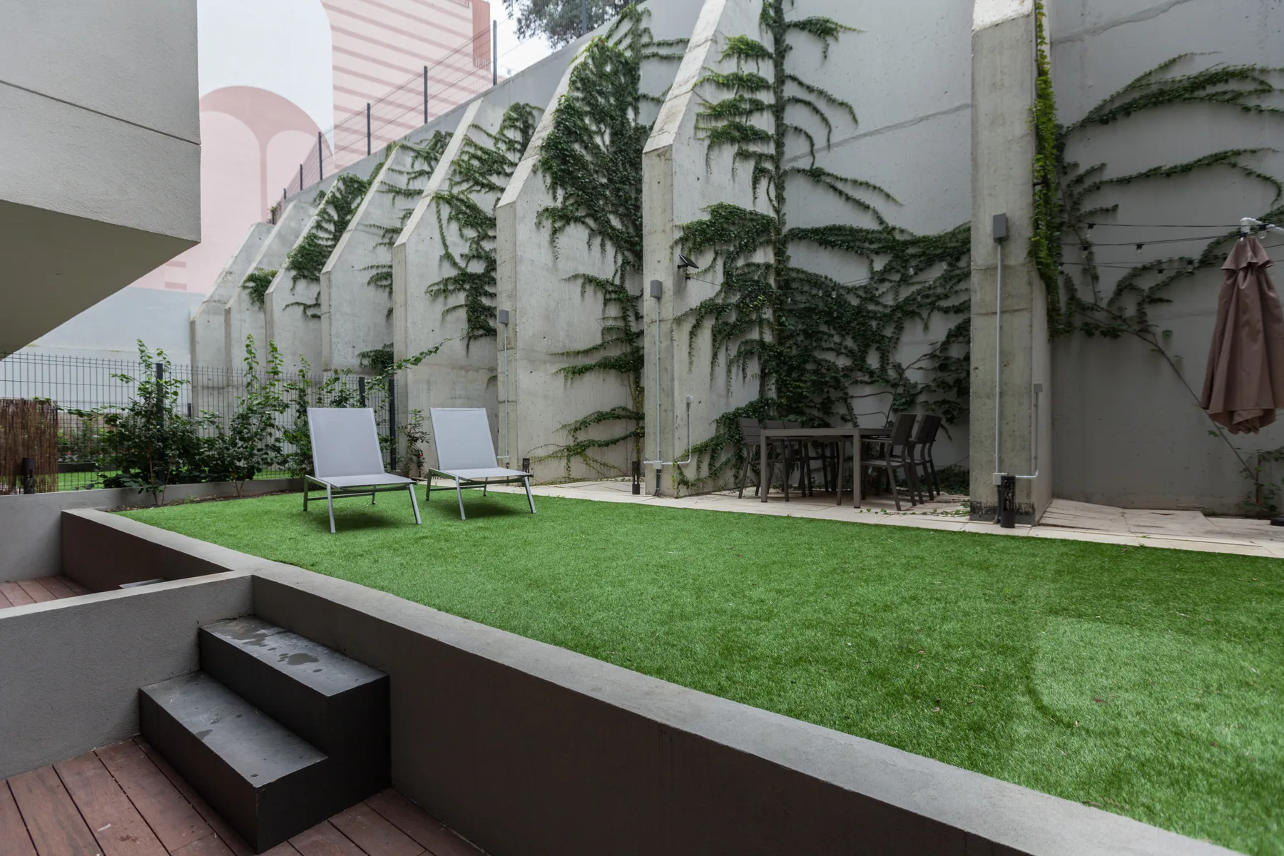 Un patio con césped artificial, asientos al aire libre y plantas trepadoras junto a las paredes.