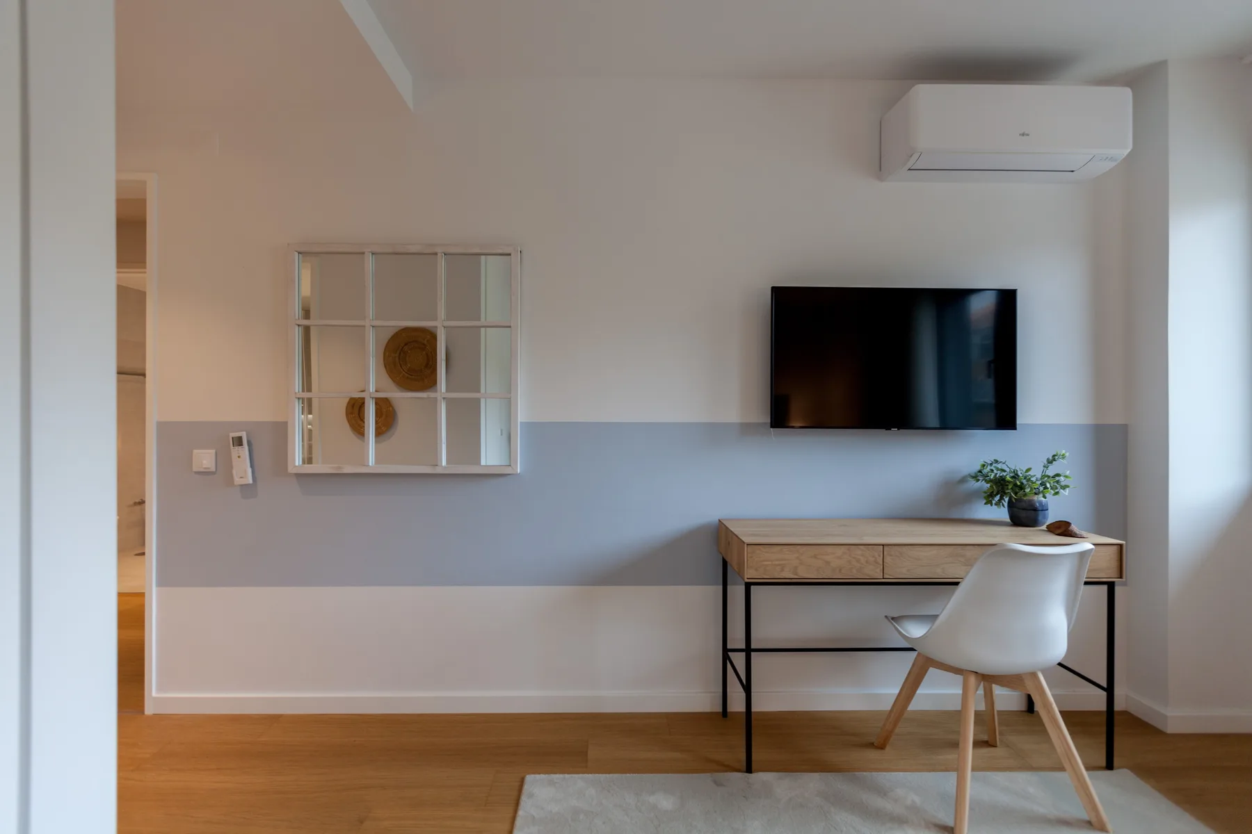 Una habitación luminosa con escritorio, asiento y televisor en la pared.