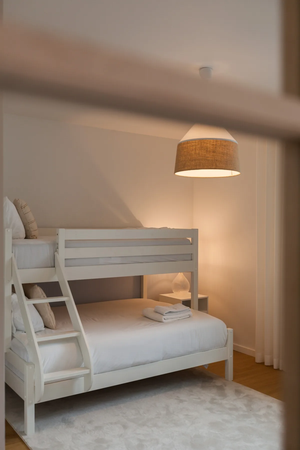 Un dormitorio con una litera blanca y una lámpara colgante.