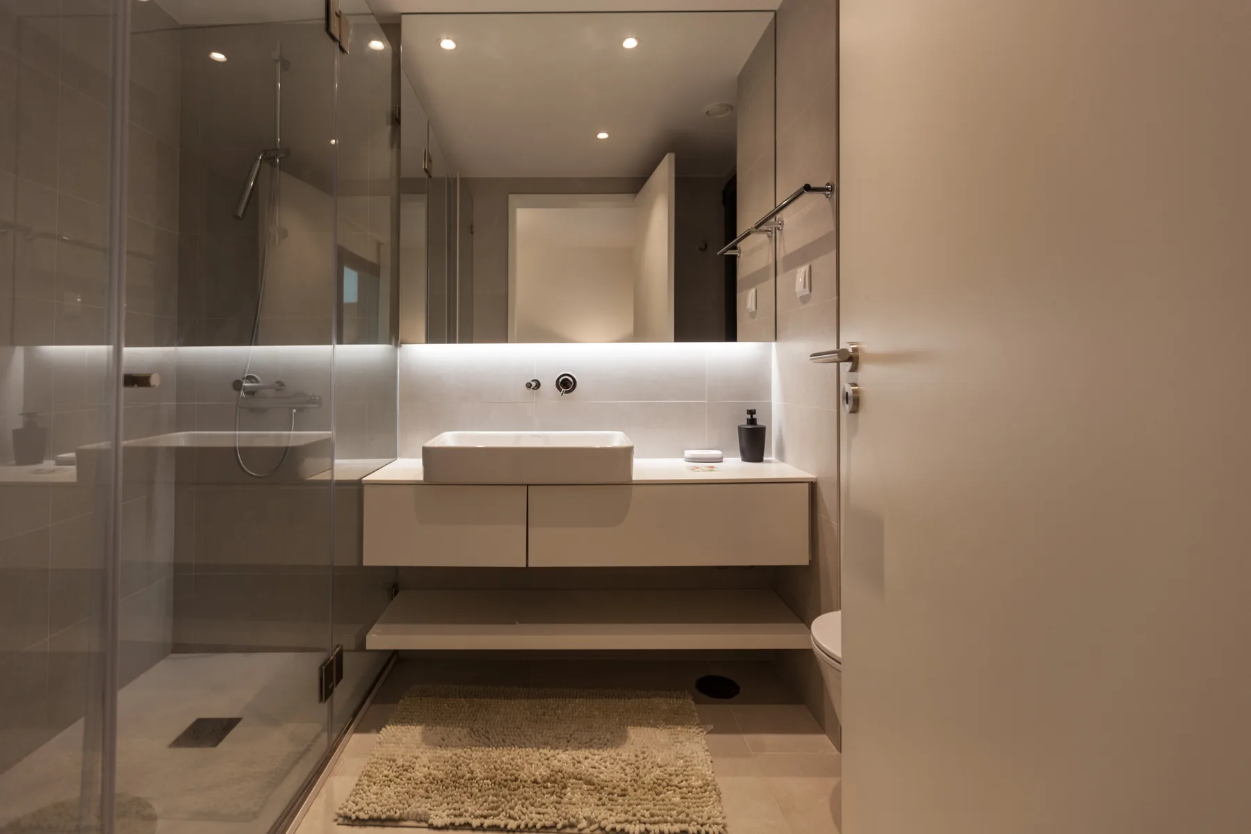 Un baño moderno con ducha de vidrio y lavabo sobre un mueble.