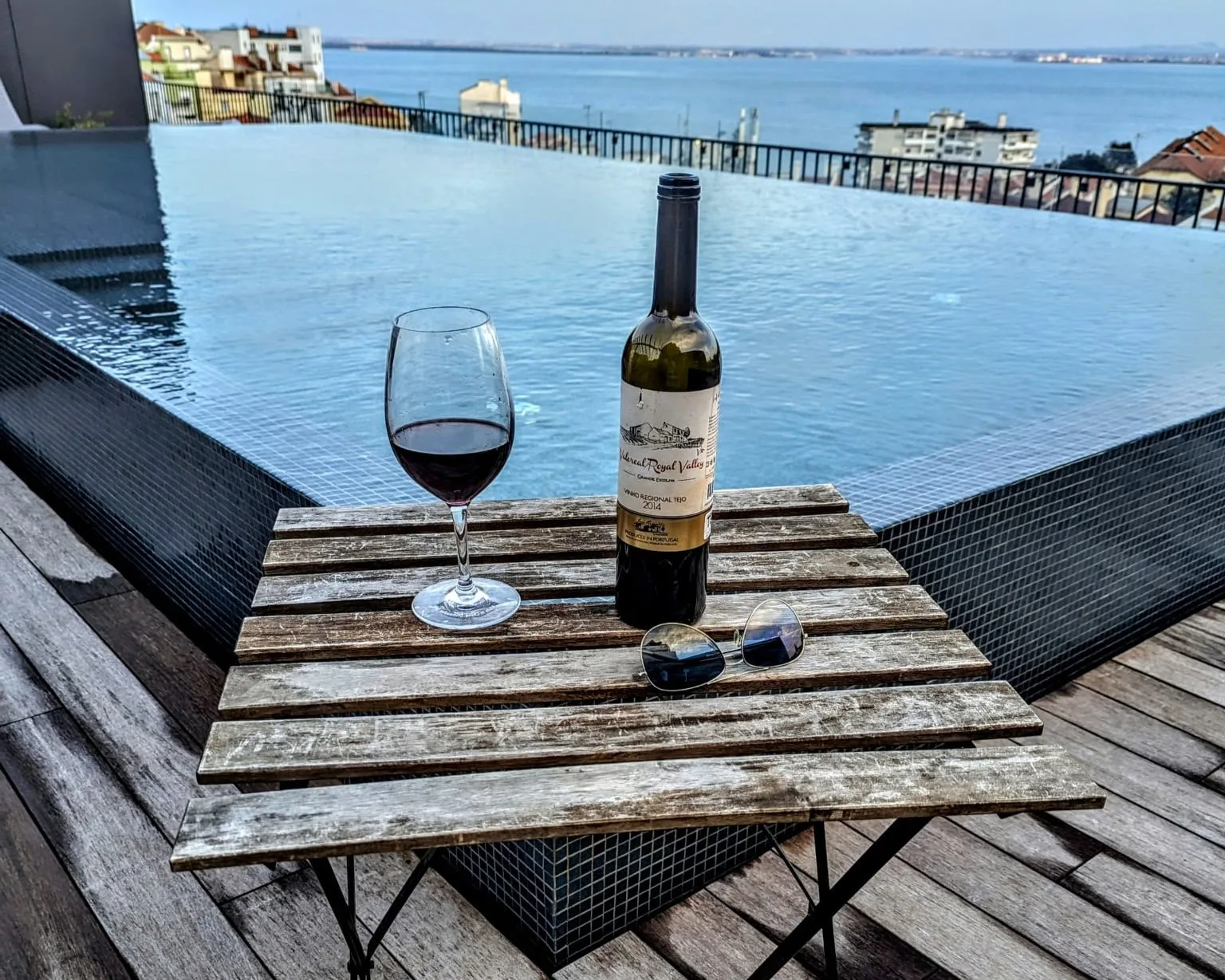 Una mesa en la terraza con vino da a una piscina infinita y al paseo marítimo.