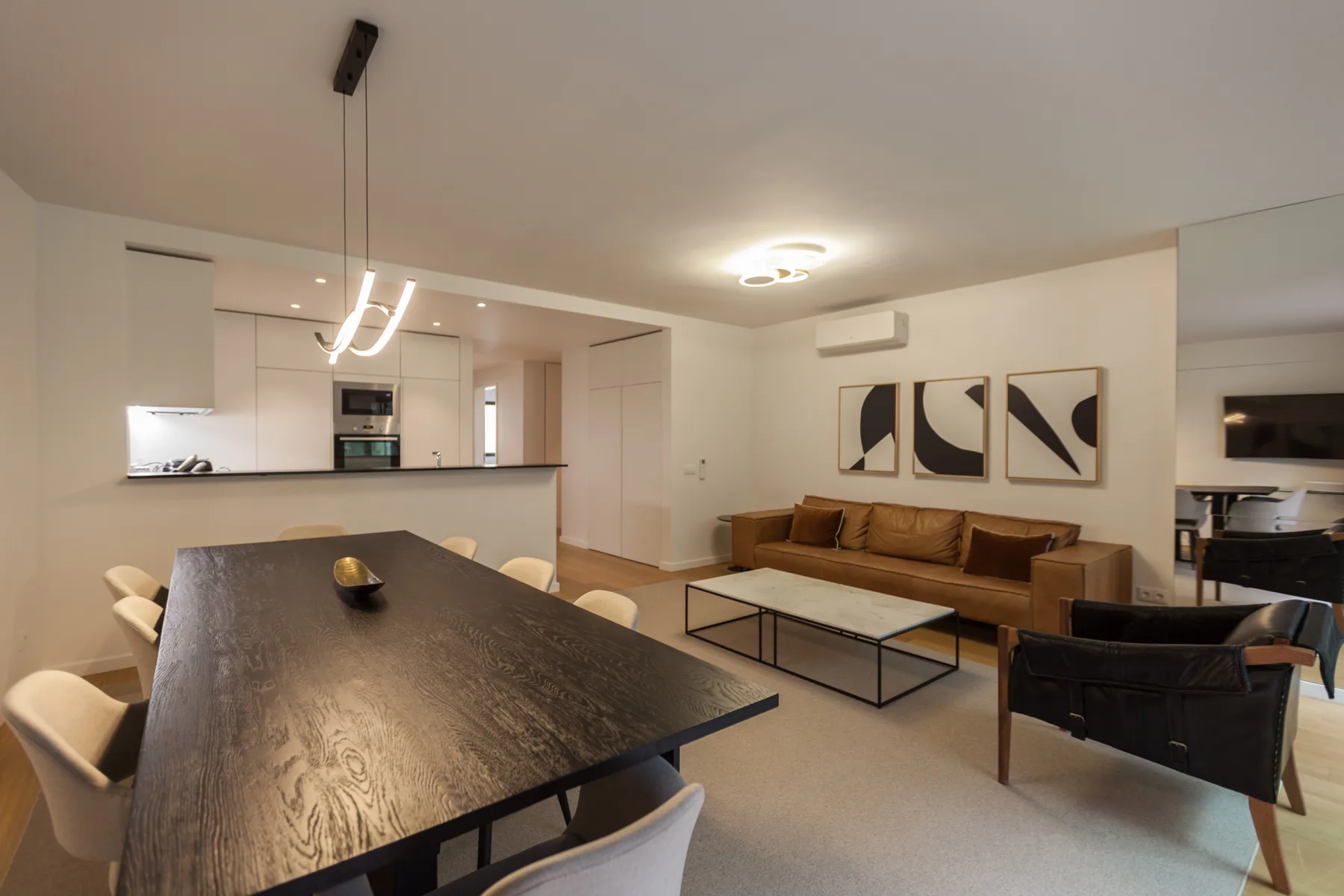 Una zona combinada de salón y comedor con una mesa larga, asientos y una cocina abierta.