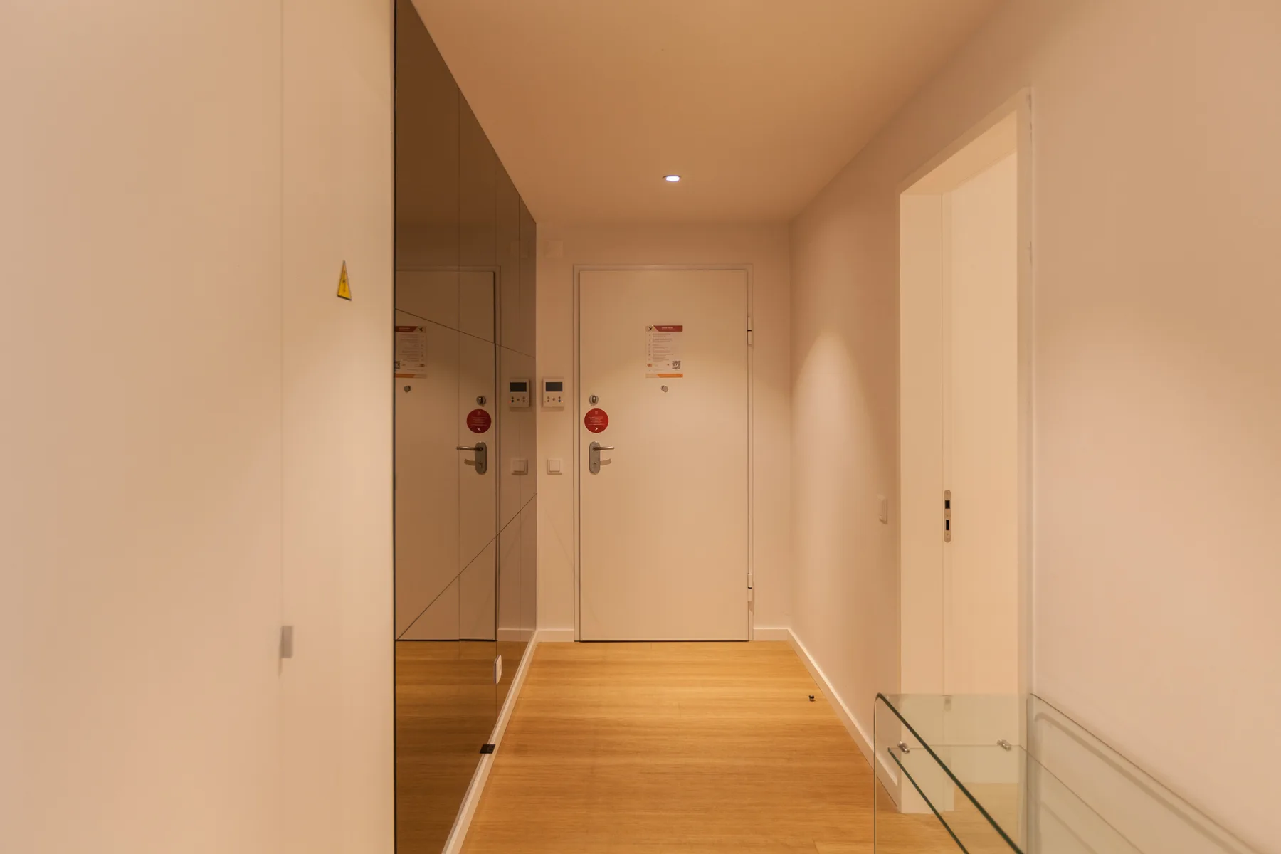 Un pasillo interior luminoso con suelo de madera y puertas.
