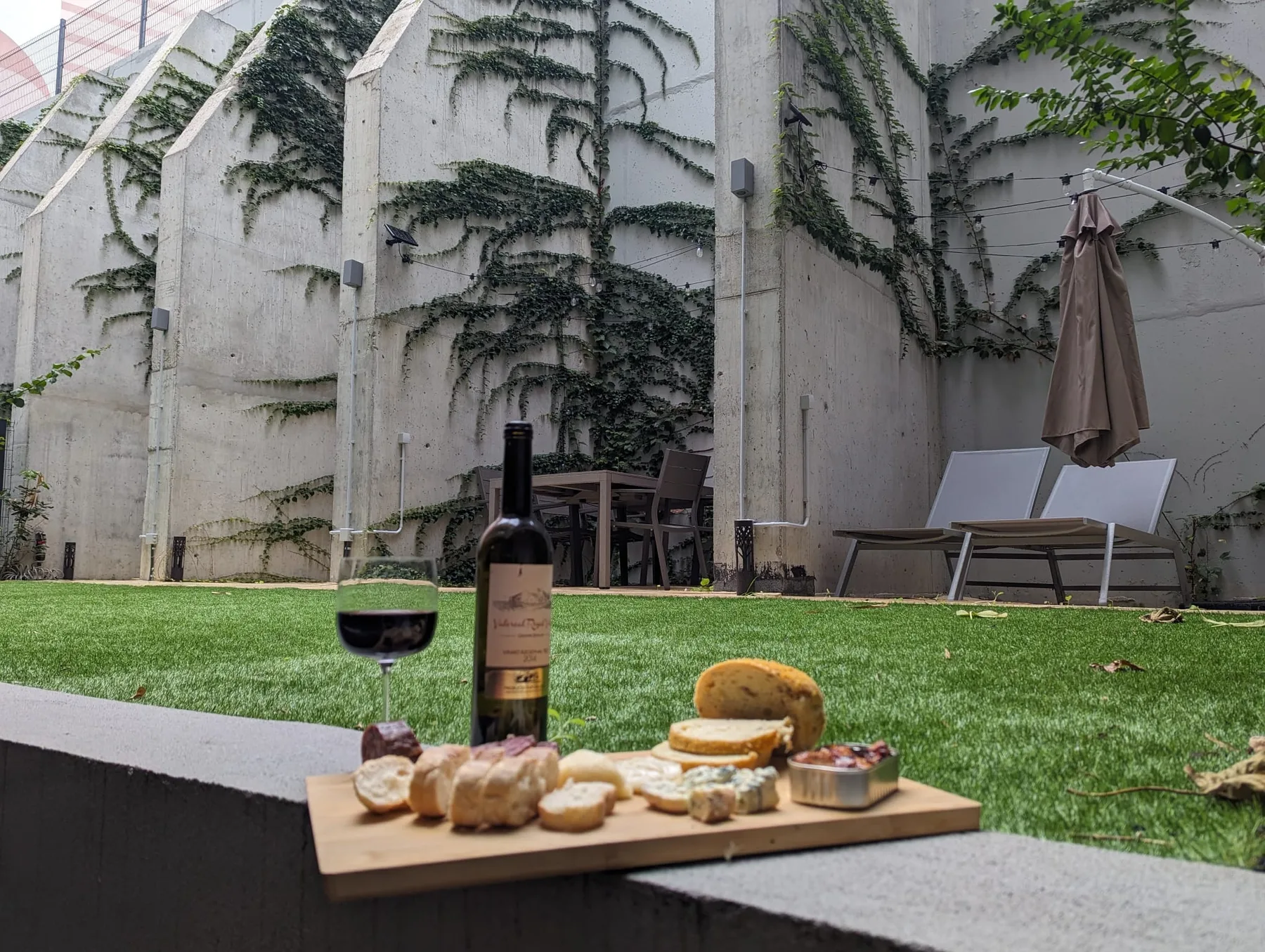 Un patio amueblado con asientos al aire libre, una sombrilla y una tabla de aperitivos junto al césped.