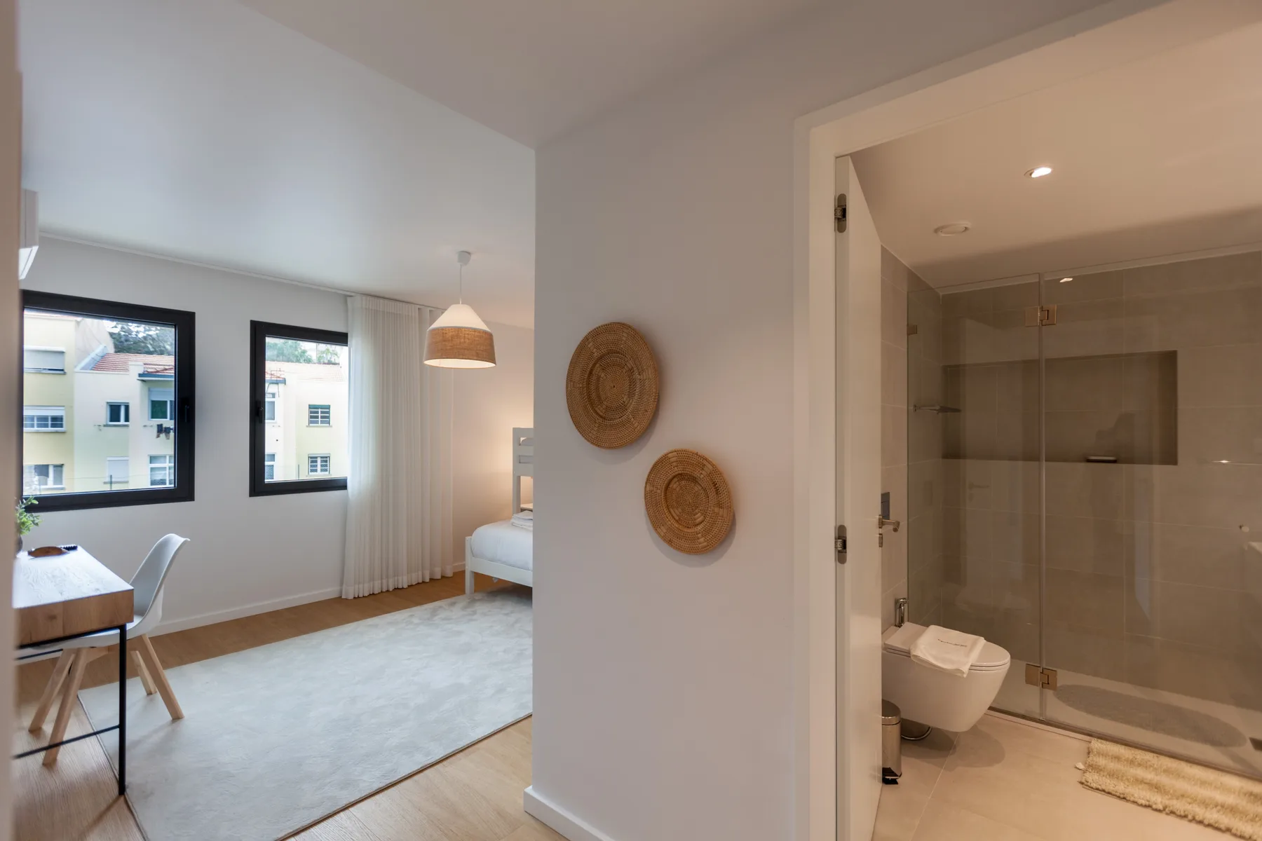 Una zona de dormitorio luminosa se abre junto a un baño con ducha de vidrio.
