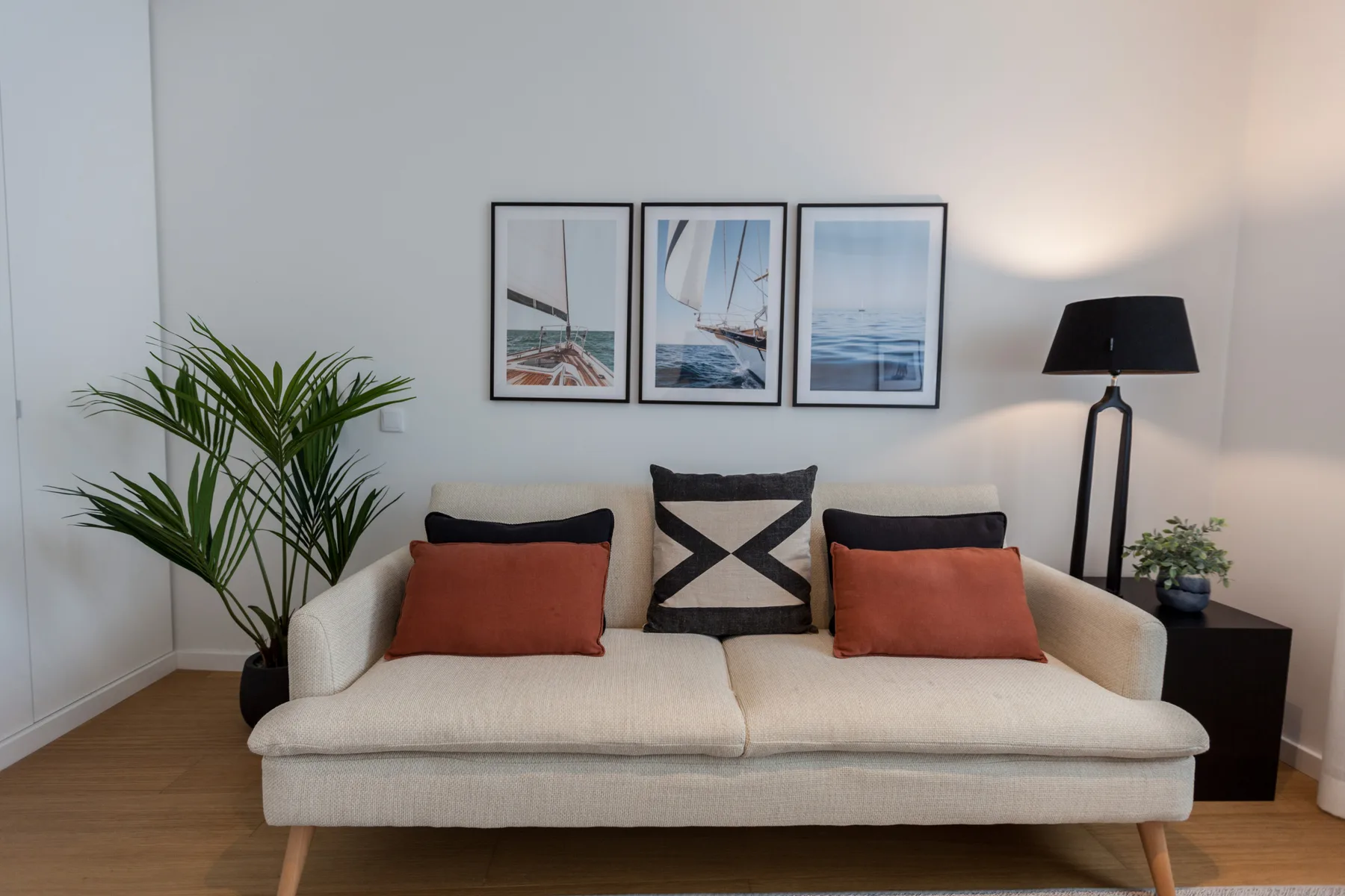 Una sala de estar con un sofá crema, cojines de colores y cuadros en la pared.