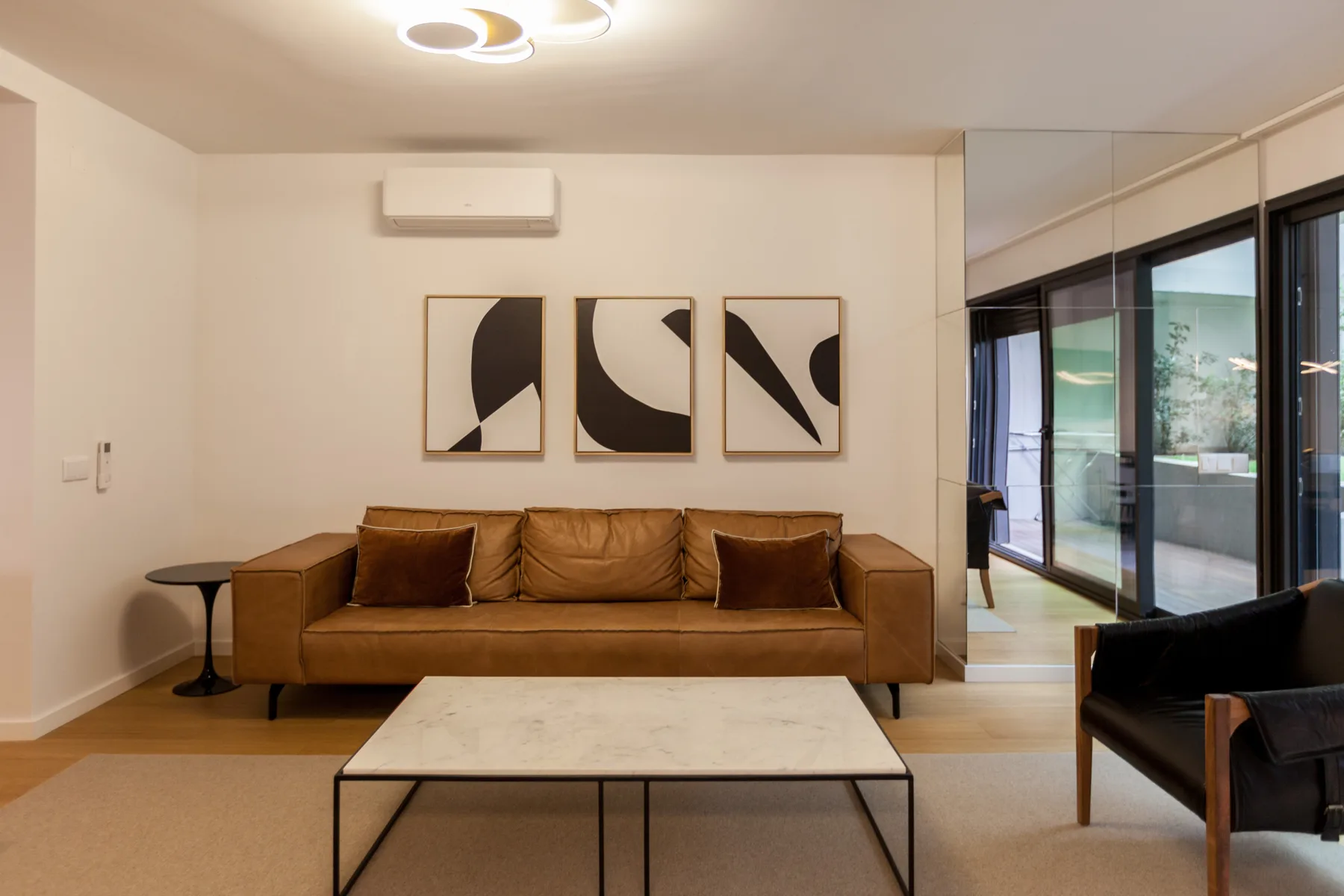 Una sala de estar moderna con un sofá marrón, arte abstracto y grandes ventanales.