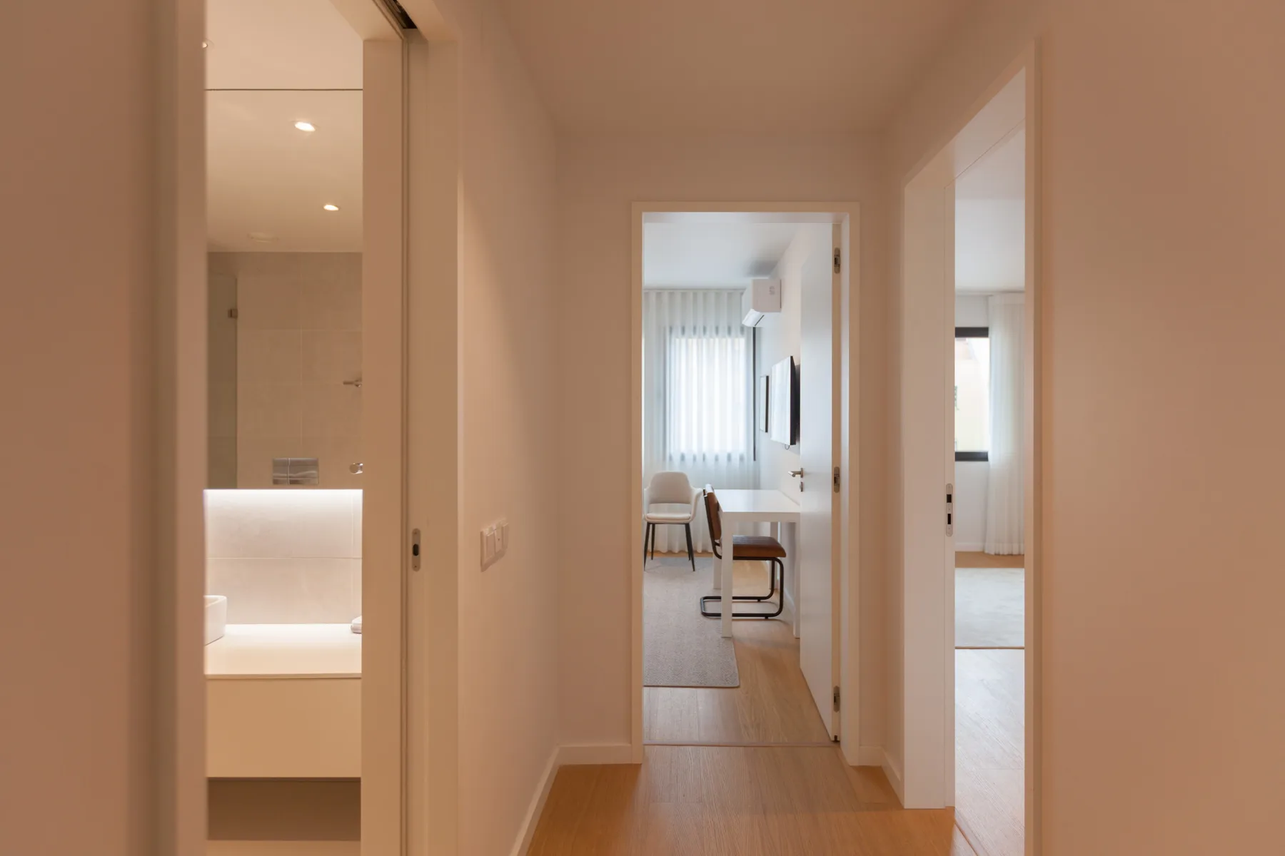 Un pasillo pasa junto a un baño abierto y conduce a una habitación luminosa con asientos.