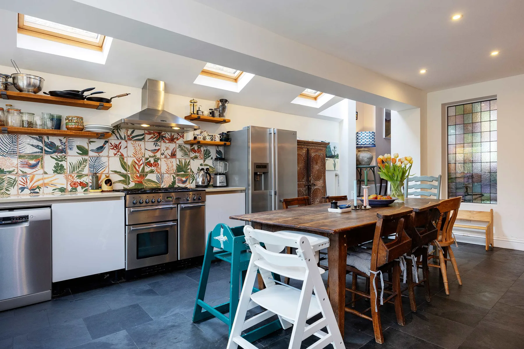 Una luminosa cocina y comedor con una mesa larga de madera y un colorido revestimiento de azulejos.