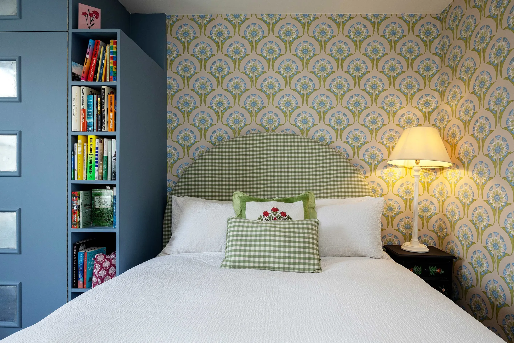 Un dormitorio con una cama vestida de blanco y una pared con papel pintado estampado.