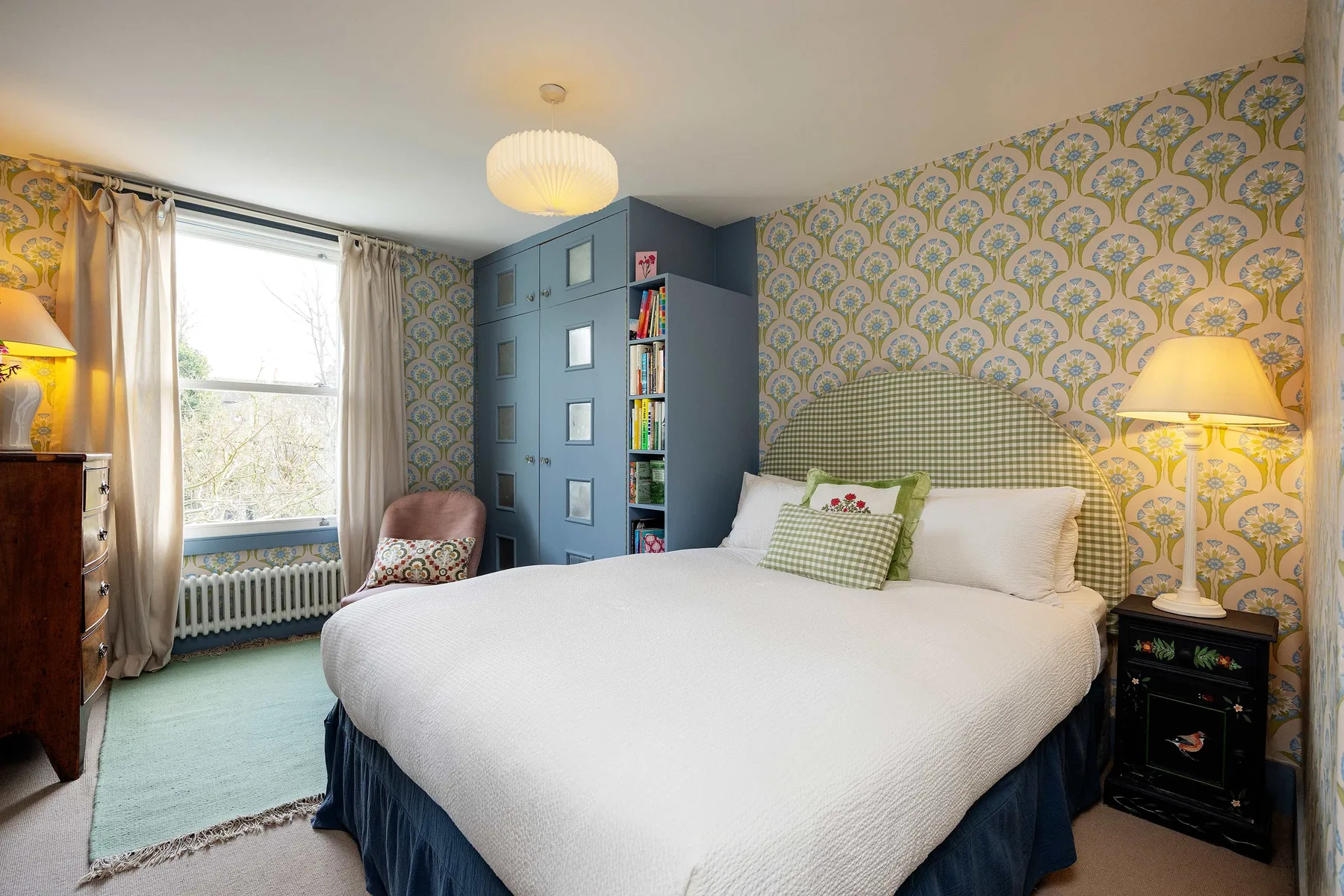 A bedroom with a large bed, patterned wallpaper, and a window.