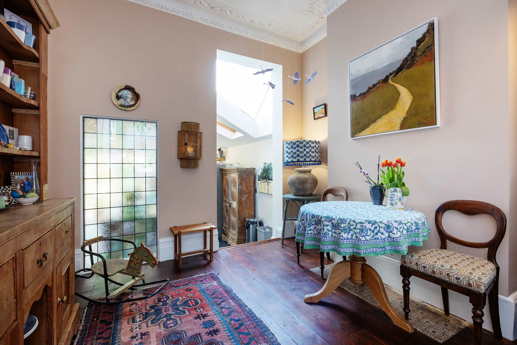 Un comedor con un mantel estampado y un cuadro de paisaje enmarcado.