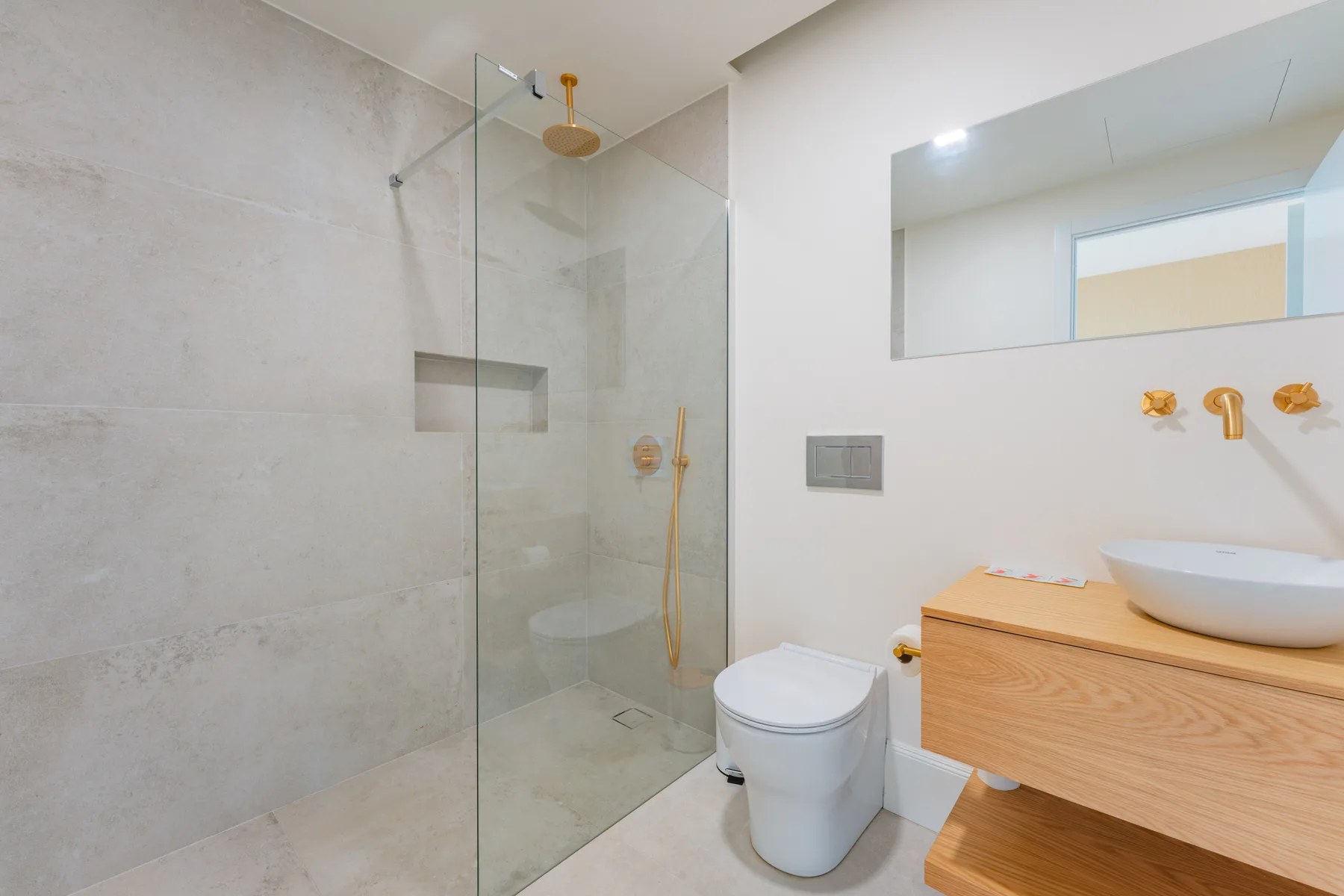 A modern bathroom with a glass shower, toilet, and wooden vanity.
