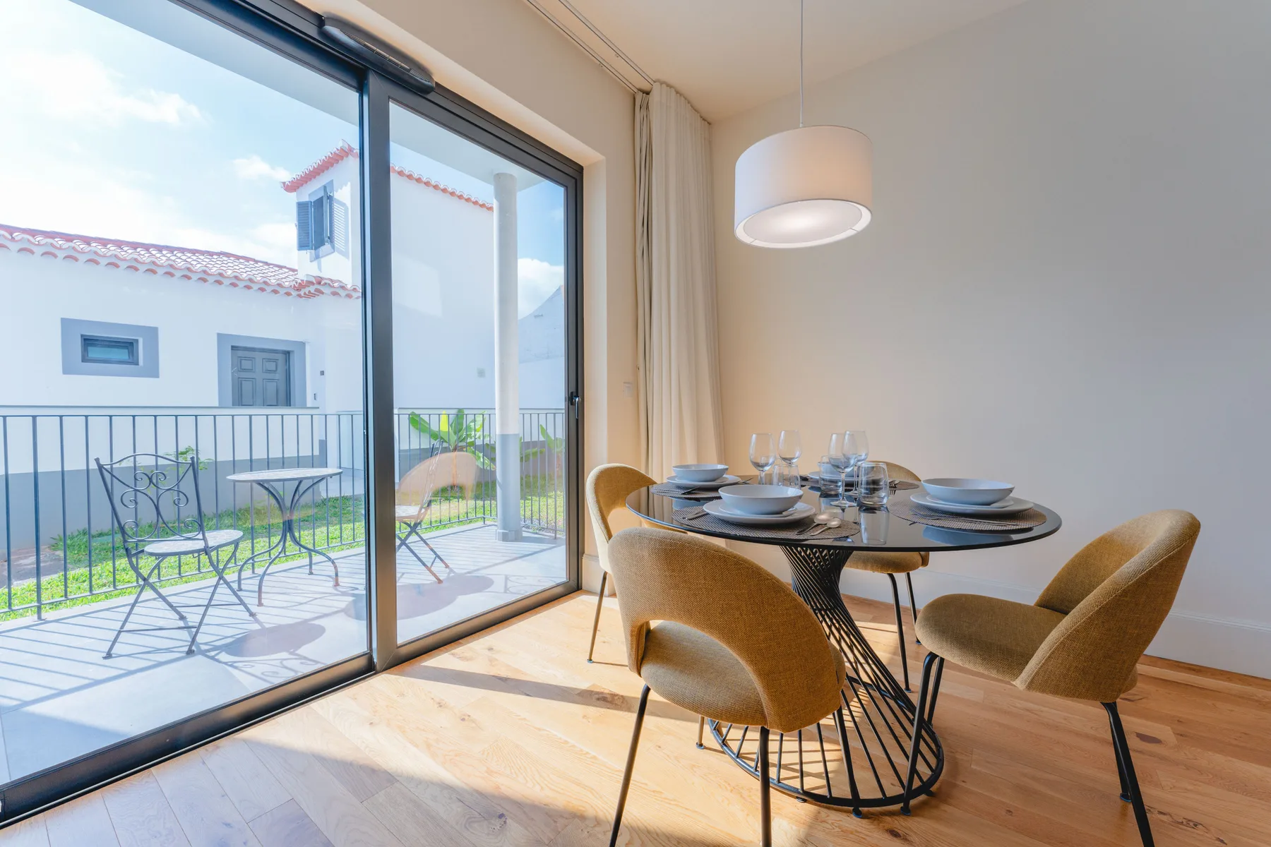 A dining area with a set table beside large glass doors opening onto a balcony.