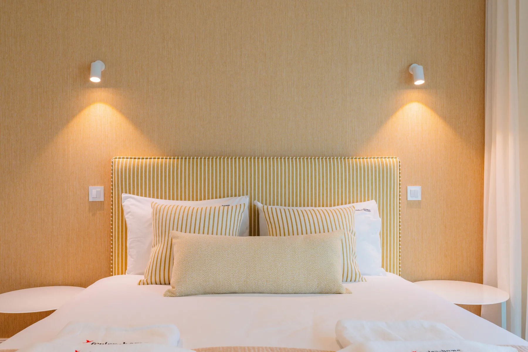 A bedroom with a neatly made bed beneath two wall lights.