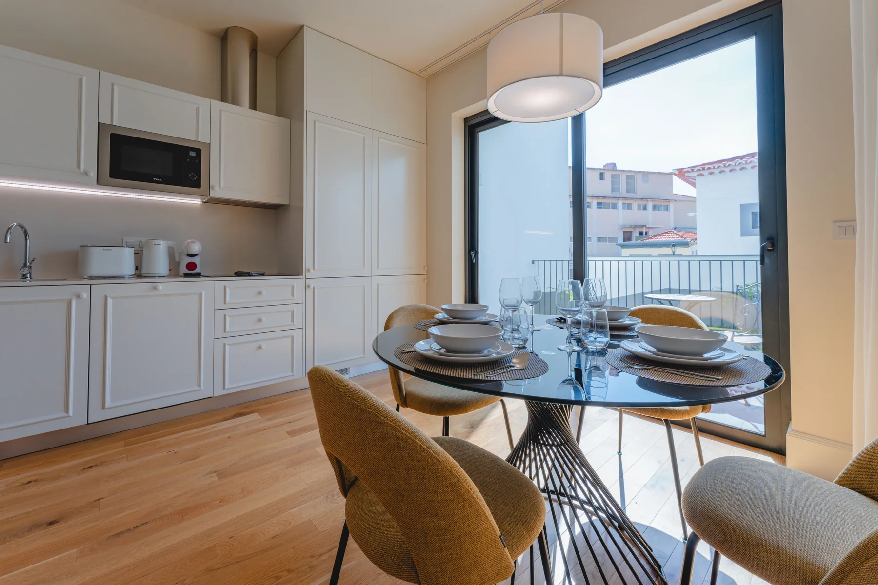 A dining area with a glass table beside a large window opening onto a balcony.