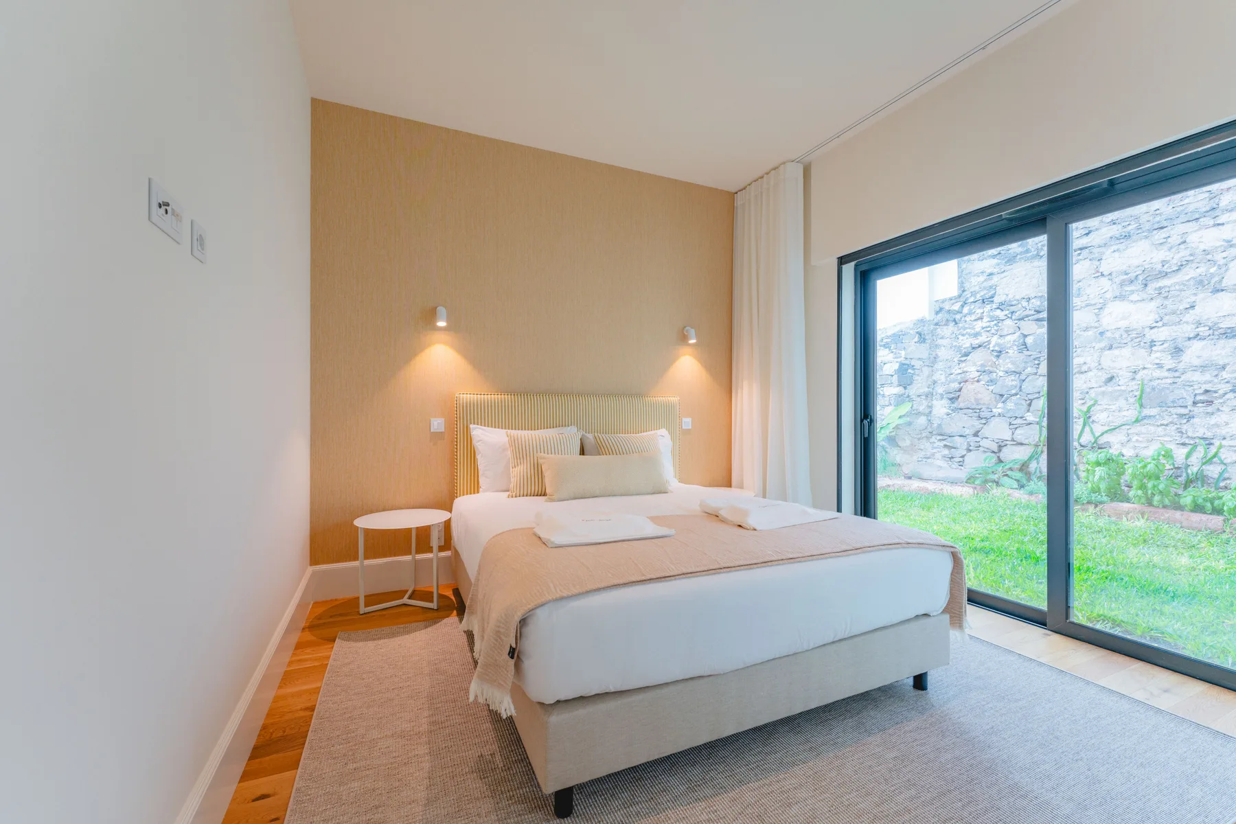 A bedroom with a bed beside large glass doors opening onto a garden.