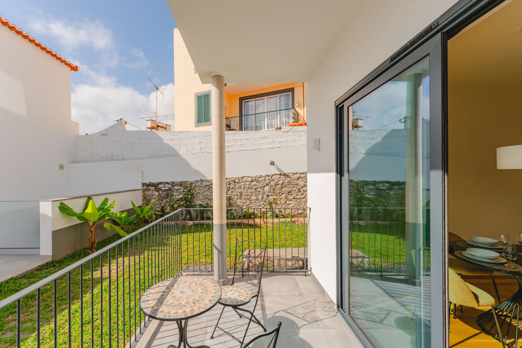 A tiled balcony with outdoor seating overlooks a small green garden.