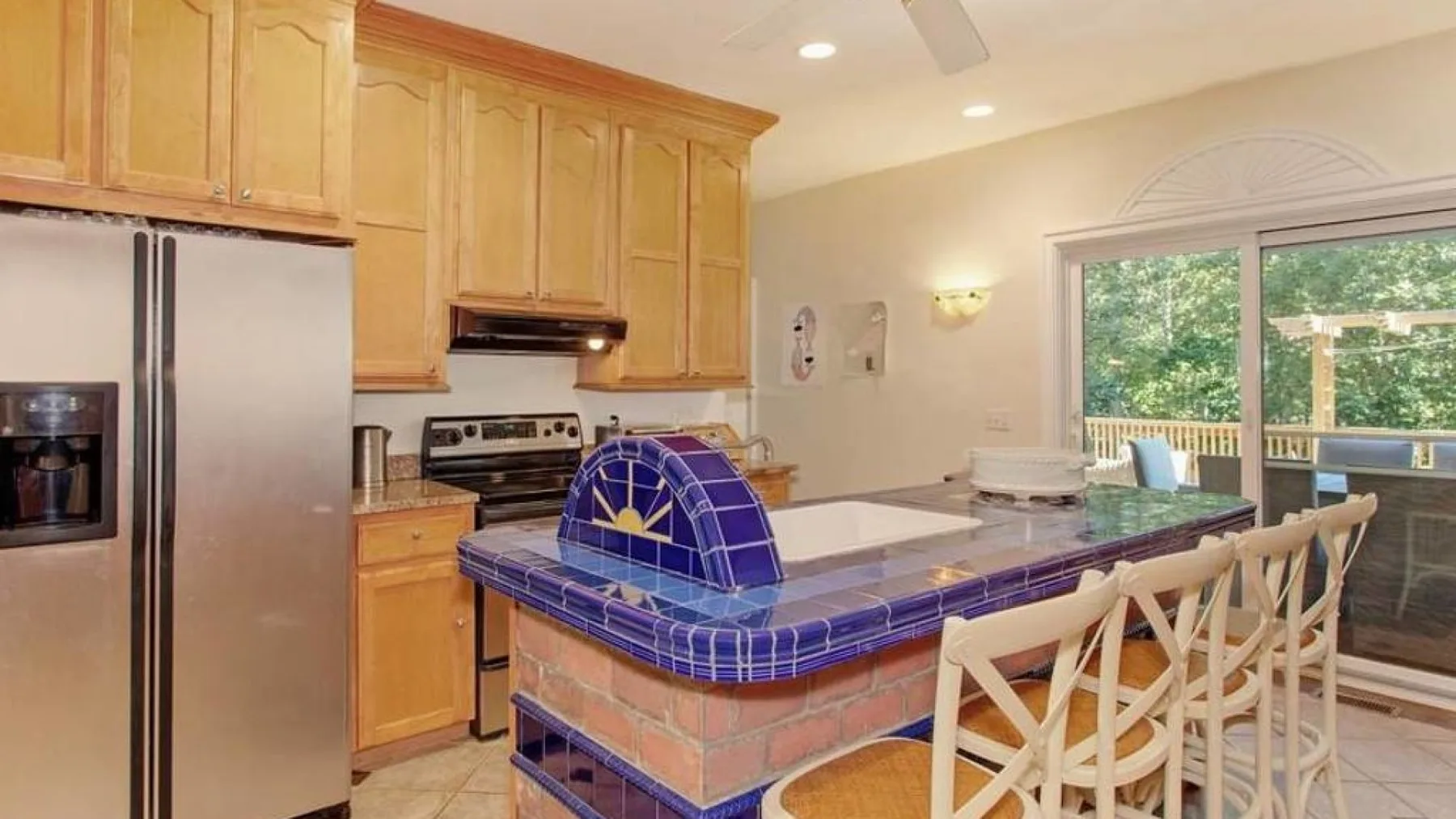 A kitchen with a blue-tiled island and light wood cabinets.