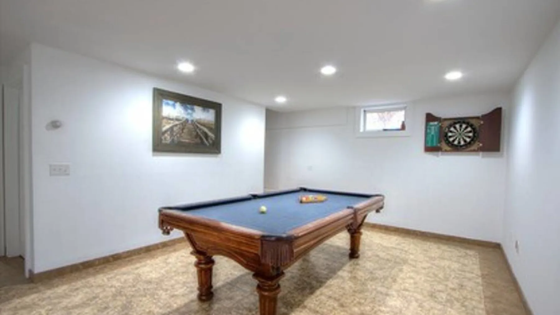 A basement game room with a pool table and a dartboard on the wall.
