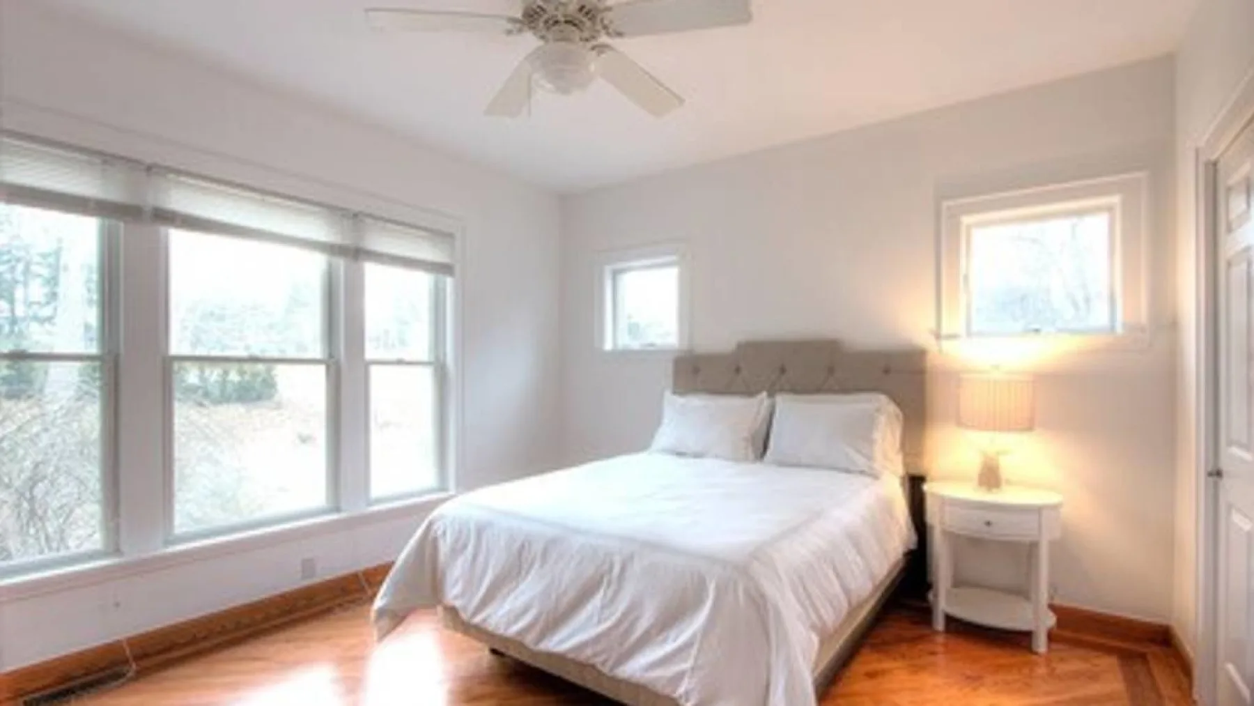 A bright bedroom with a bed beside large windows and a bedside table.