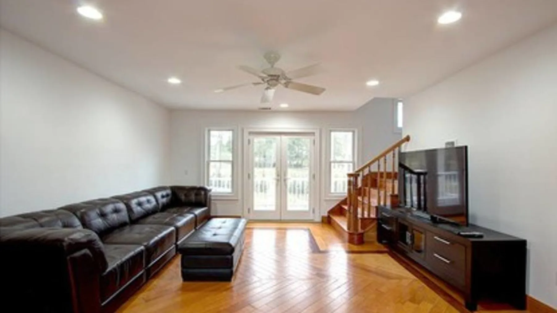A living room with dark seating, a television, and glass doors.