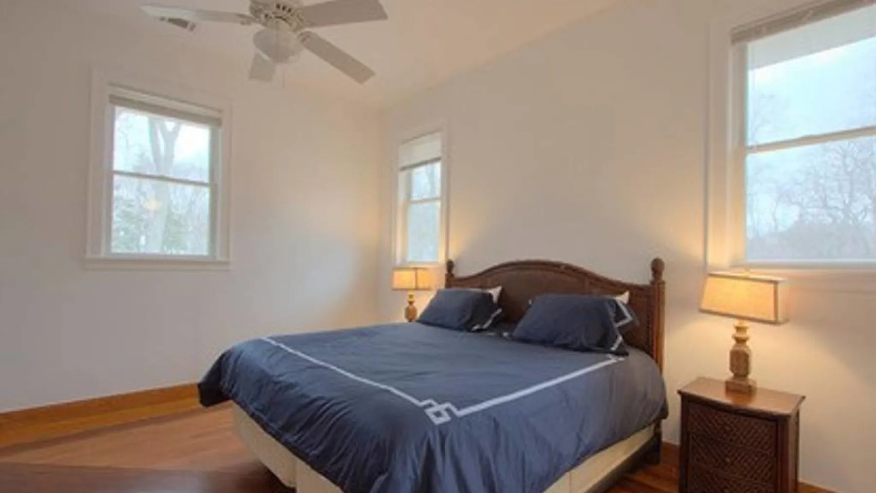 A bedroom with a bed, bedside lamps, and windows.