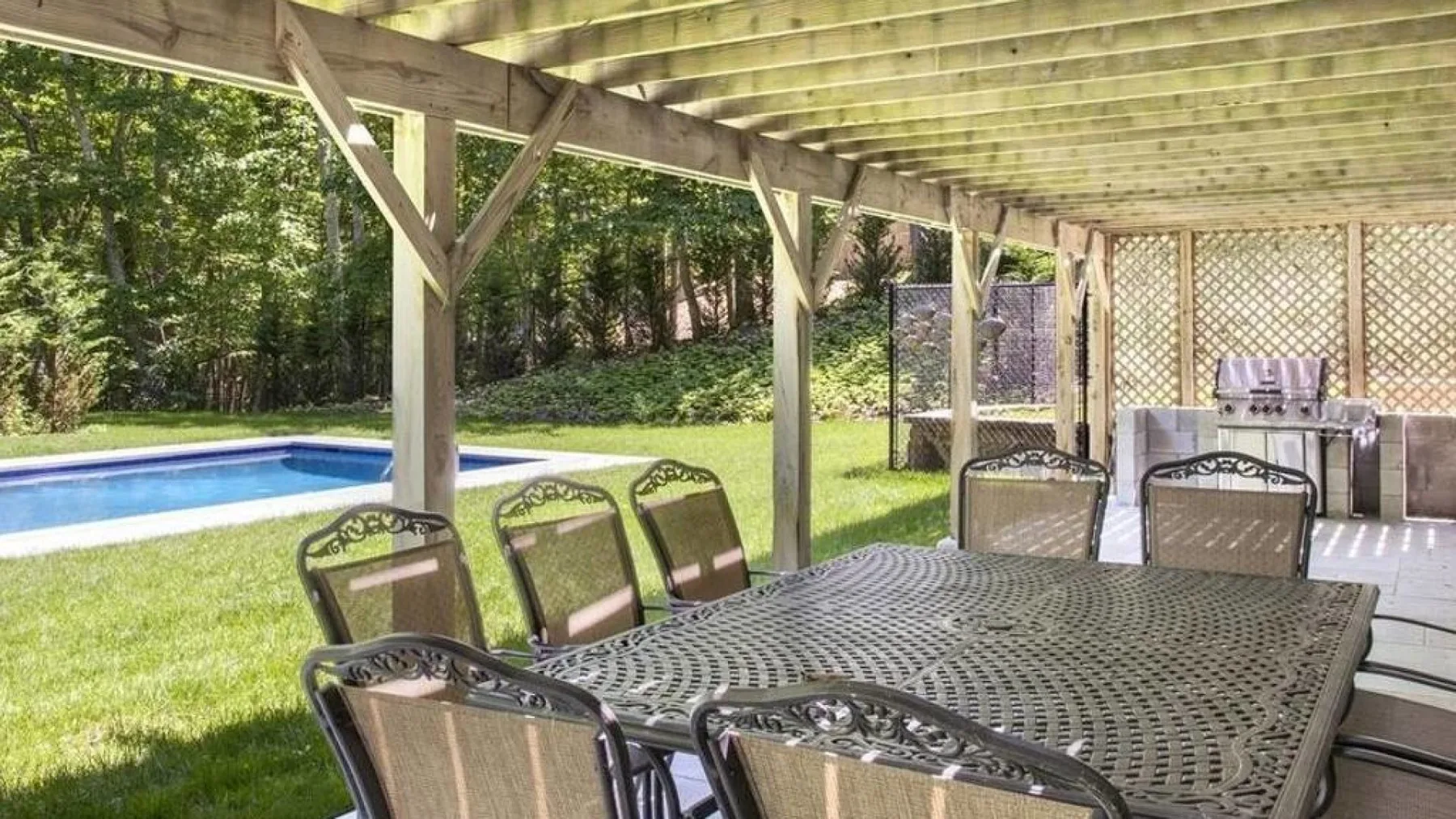 A covered outdoor dining area with a large table beside a swimming pool.