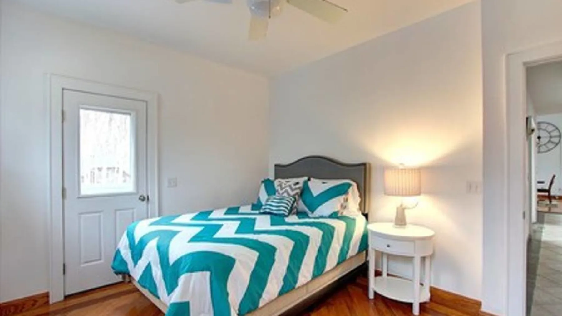 A bedroom with a bed dressed in teal and white geometric bedding beside a lit table lamp.
