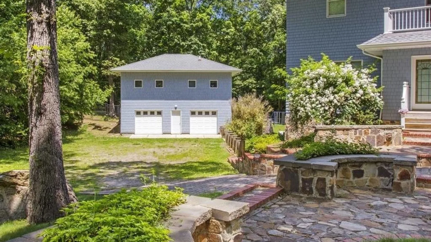 A paved outdoor patio with a stone seating area beside a house and detached garage.