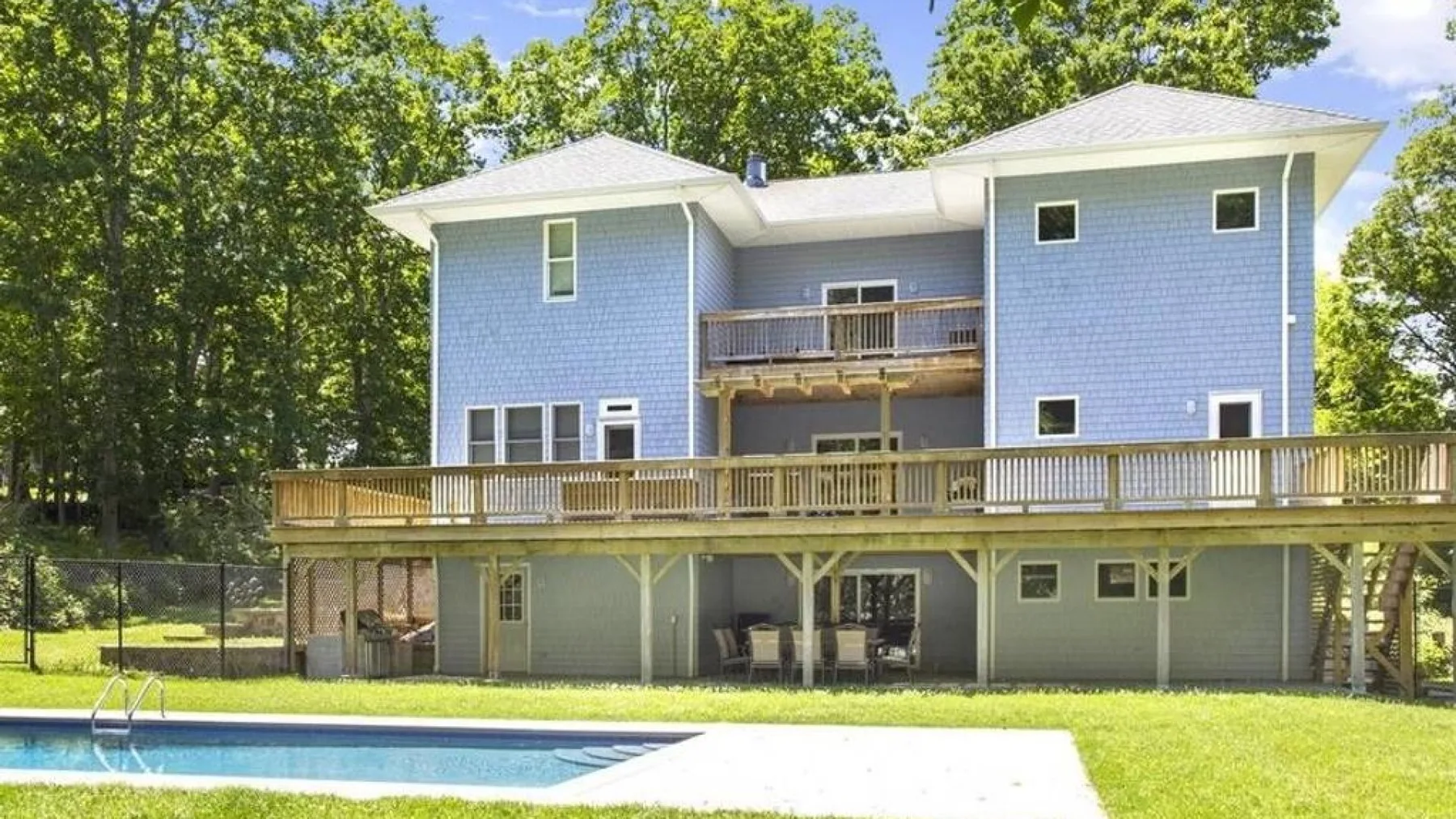 A large house with an elevated deck overlooks a backyard swimming pool.