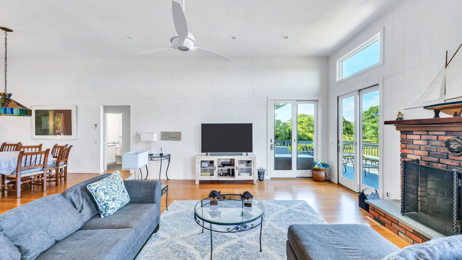 A bright living room with a seating area, television, and large windows.
