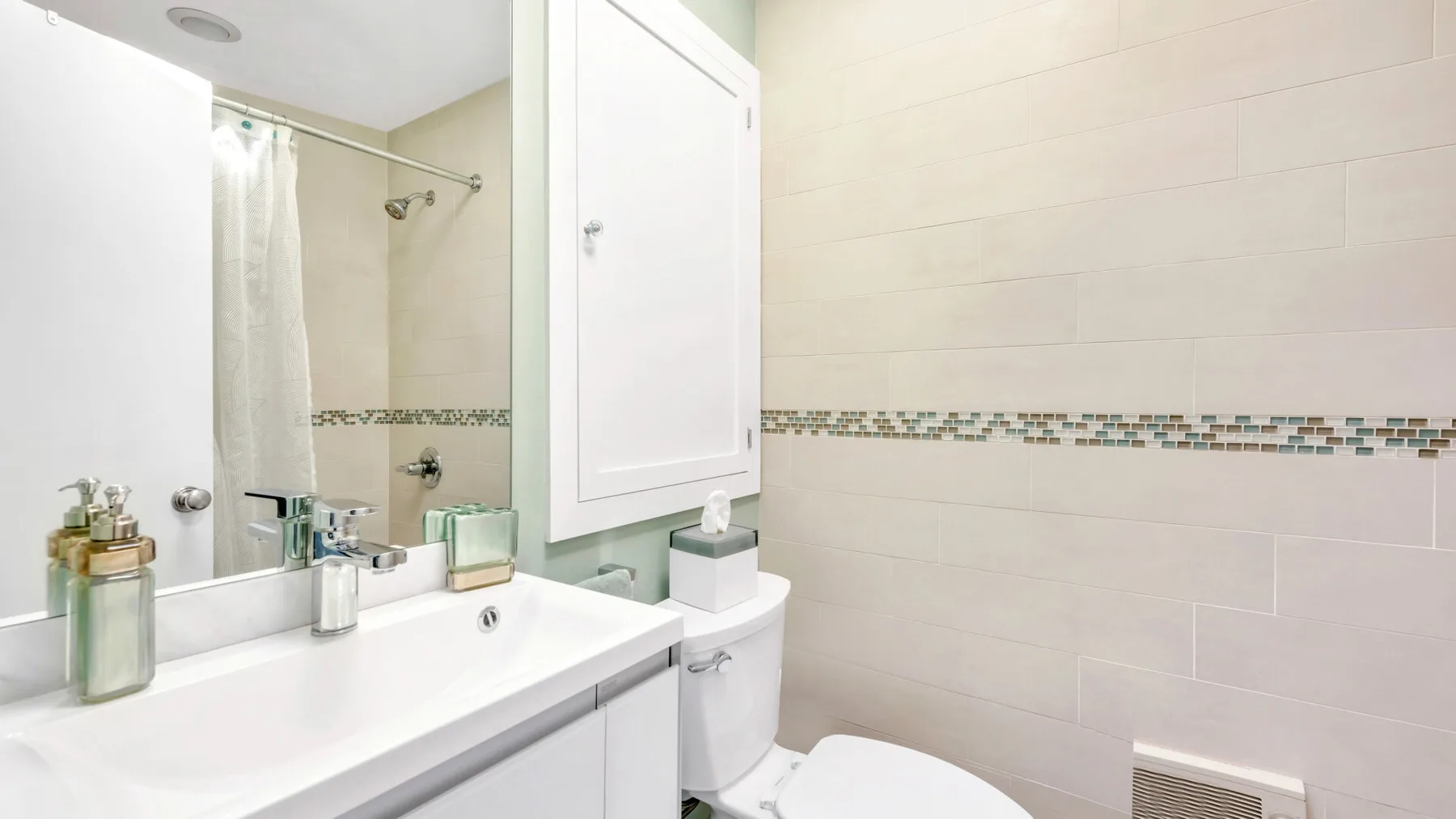 Un baño con lavabo blanco, espejo y paredes de azulejos.
