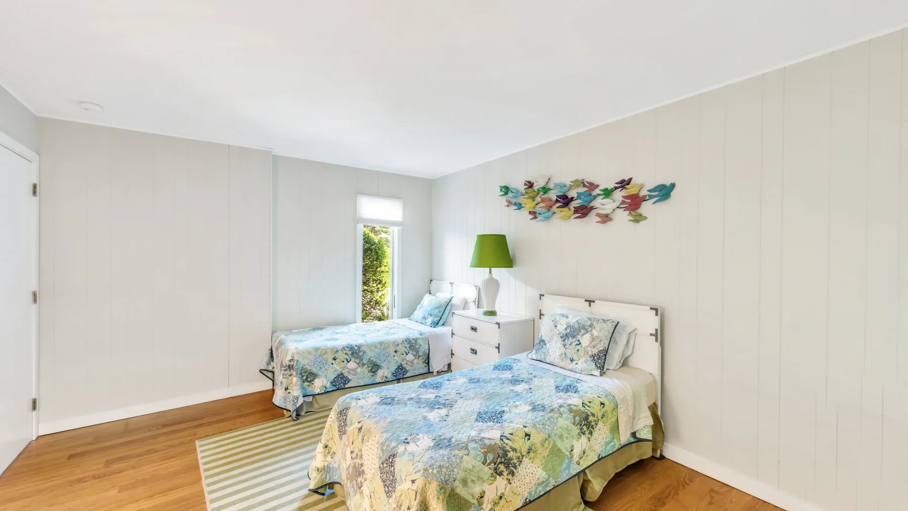 Un dormitorio luminoso con dos camas, muebles junto a ellas y arte colorido en la pared.