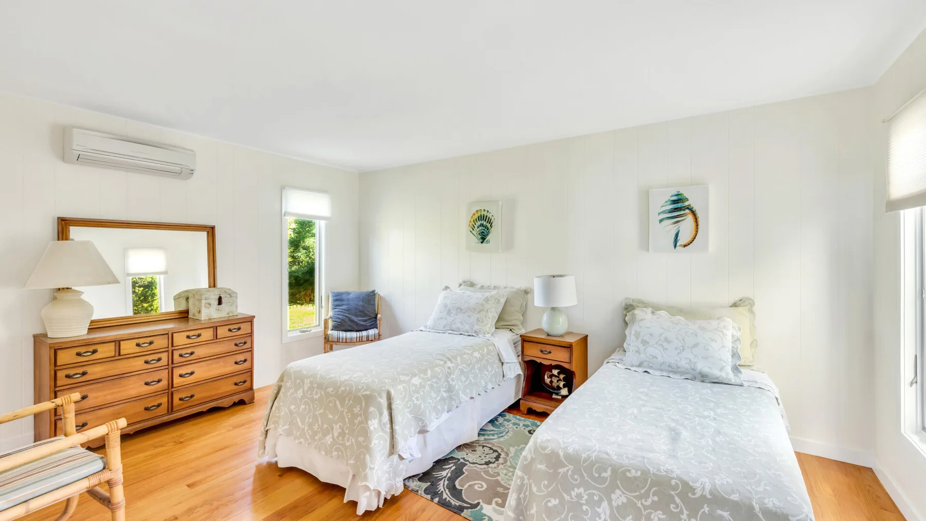 Un dormitorio luminoso con dos camas y una cómoda de madera.