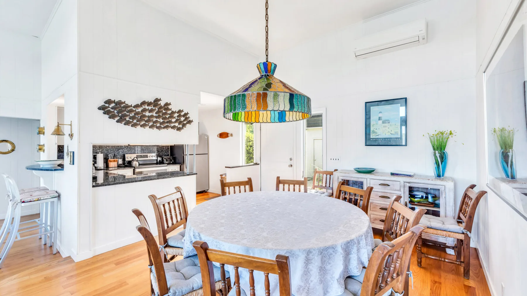 Un comedor luminoso con una mesa grande, asientos de madera y una lámpara colgante colorida.