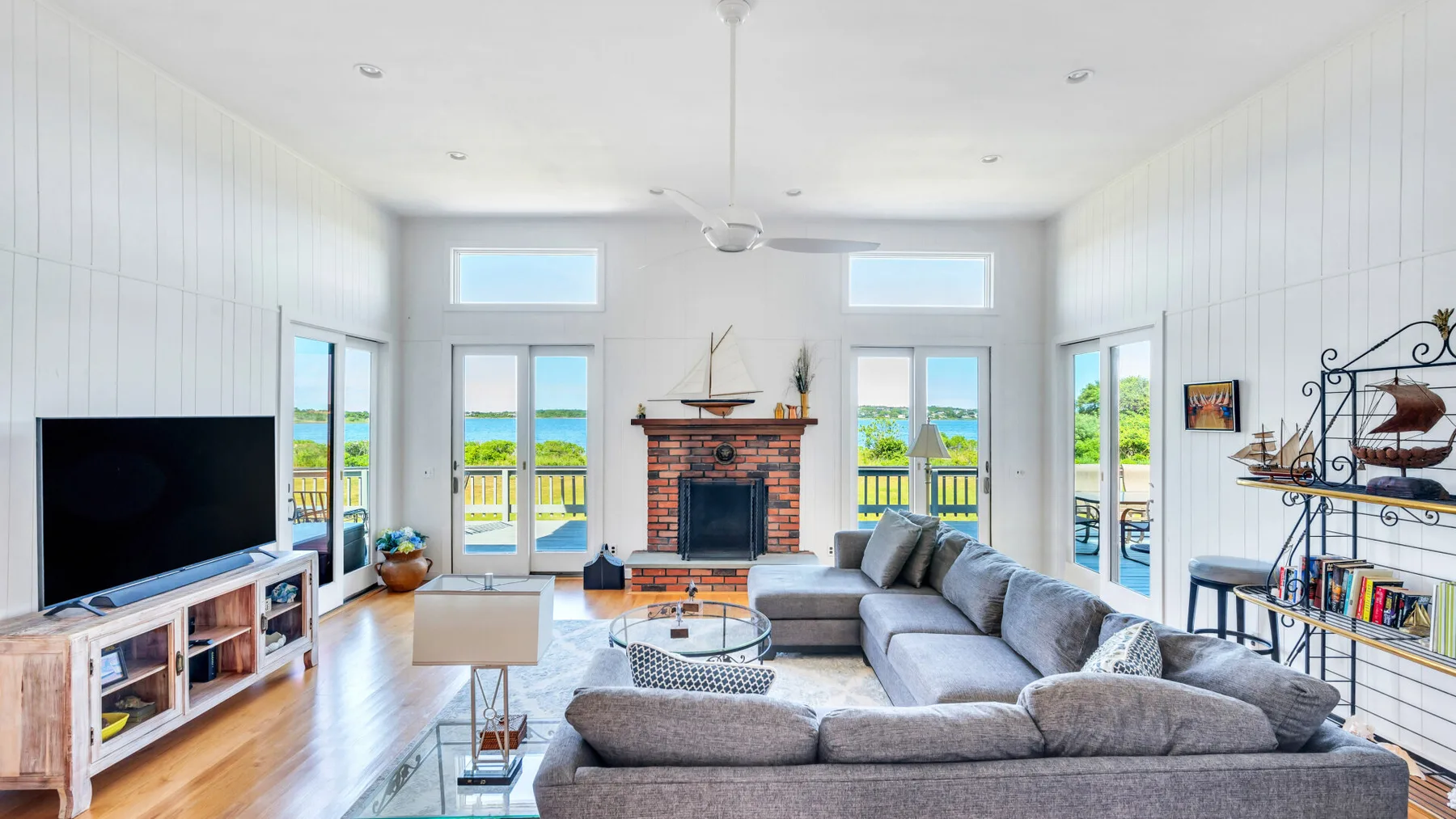 Sala de estar luminosa con un sofá seccional grande, chimenea y ventanas con vista al agua.